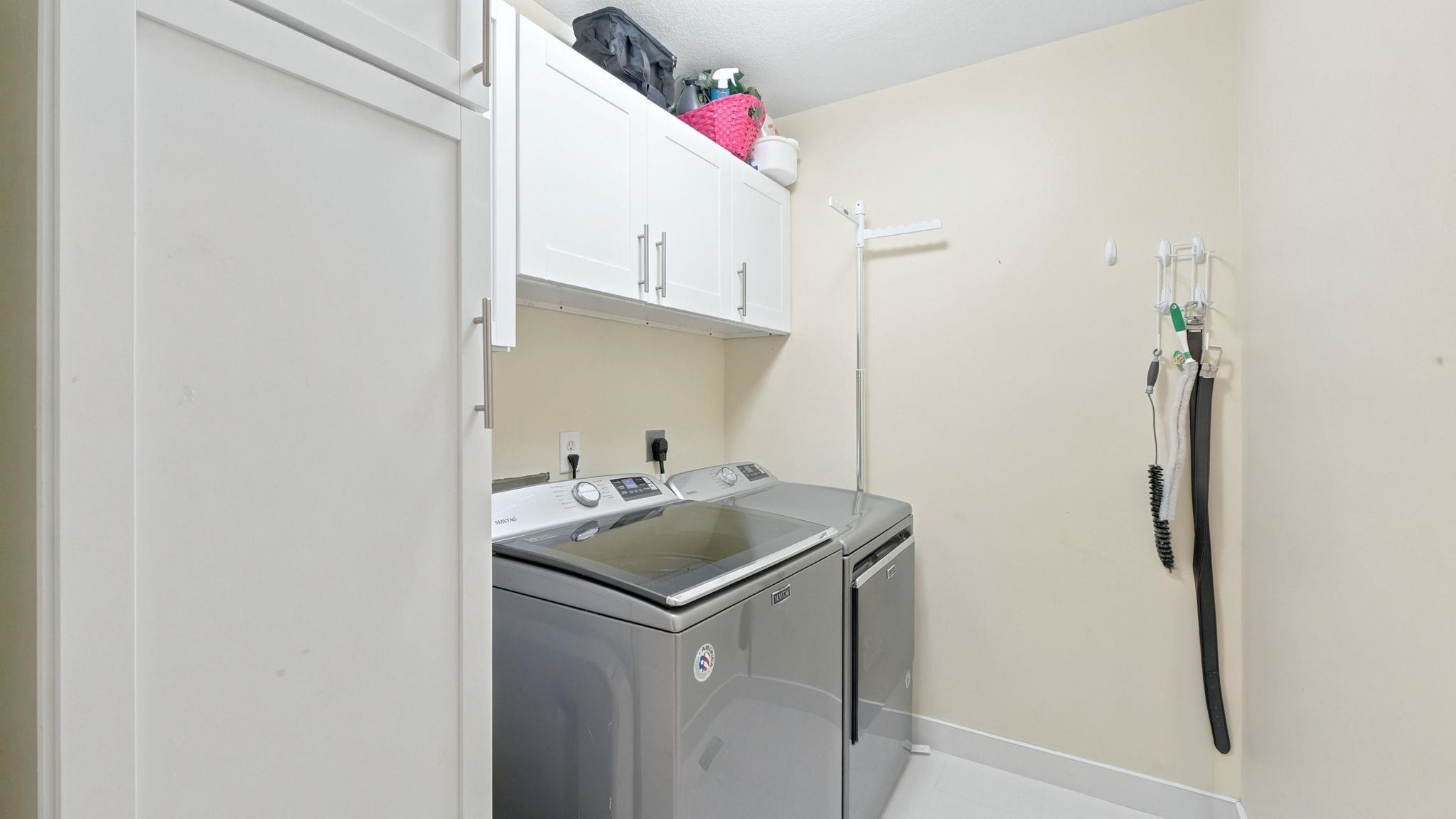 Dedicated laundry space featuring white shaker-style cabinetry, overhead storage, and light-toned walls