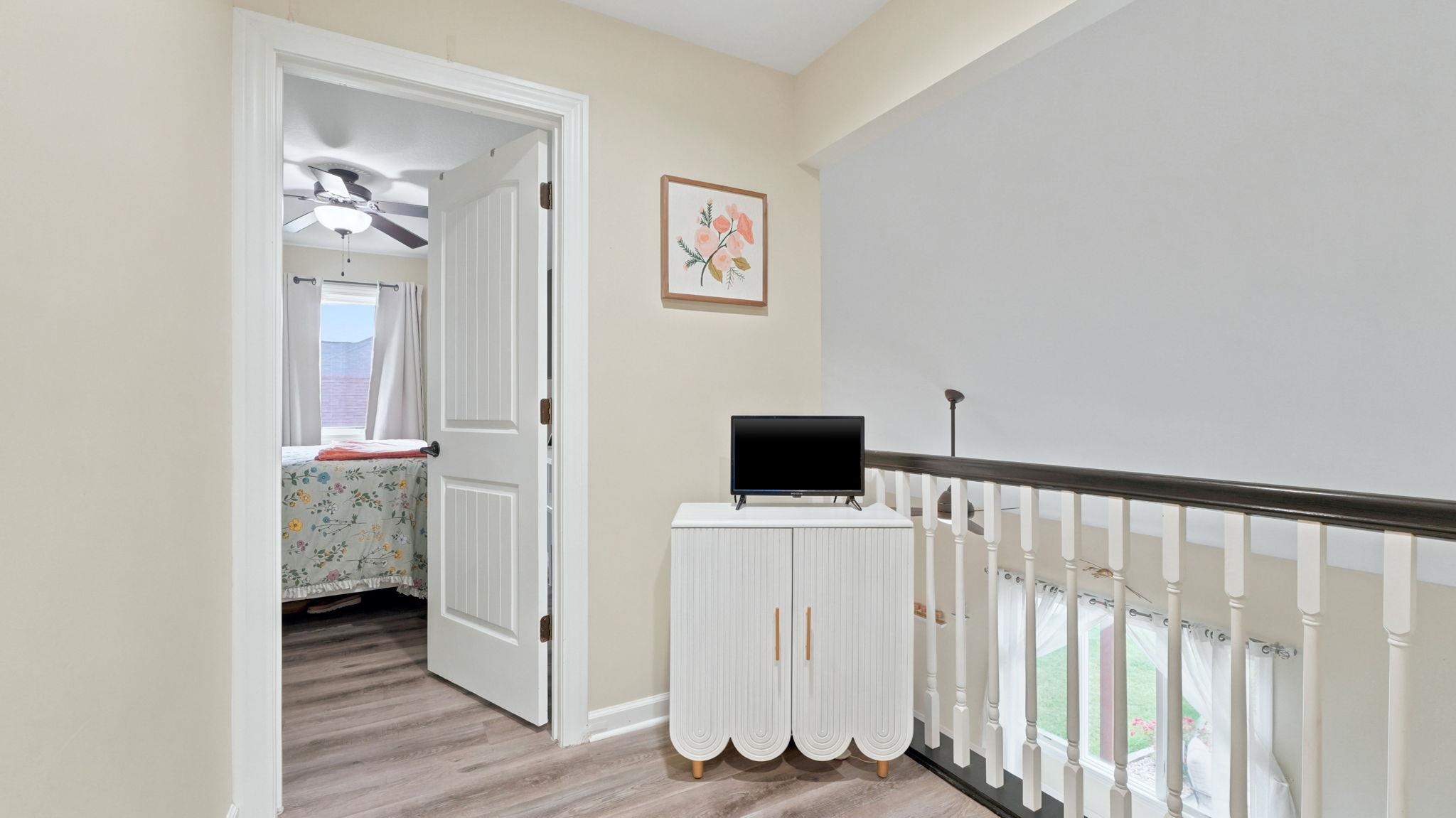 Interior hallway with wood-finish flooring, white walls, and a white balustrade with a dark top rail