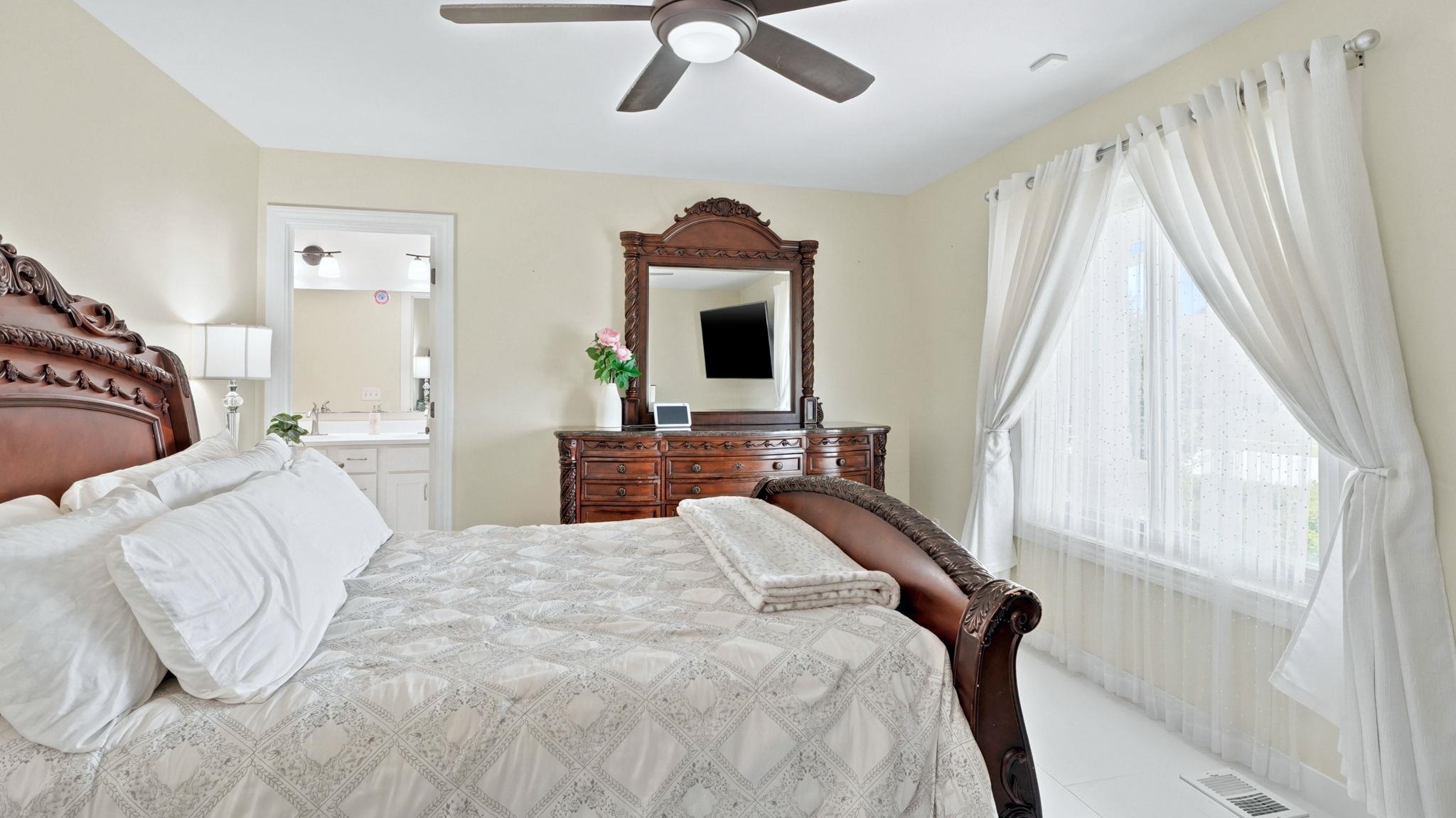 Bedroom featuring a window with sheer and blackout curtains, light-toned walls, and wood-finish flooring
