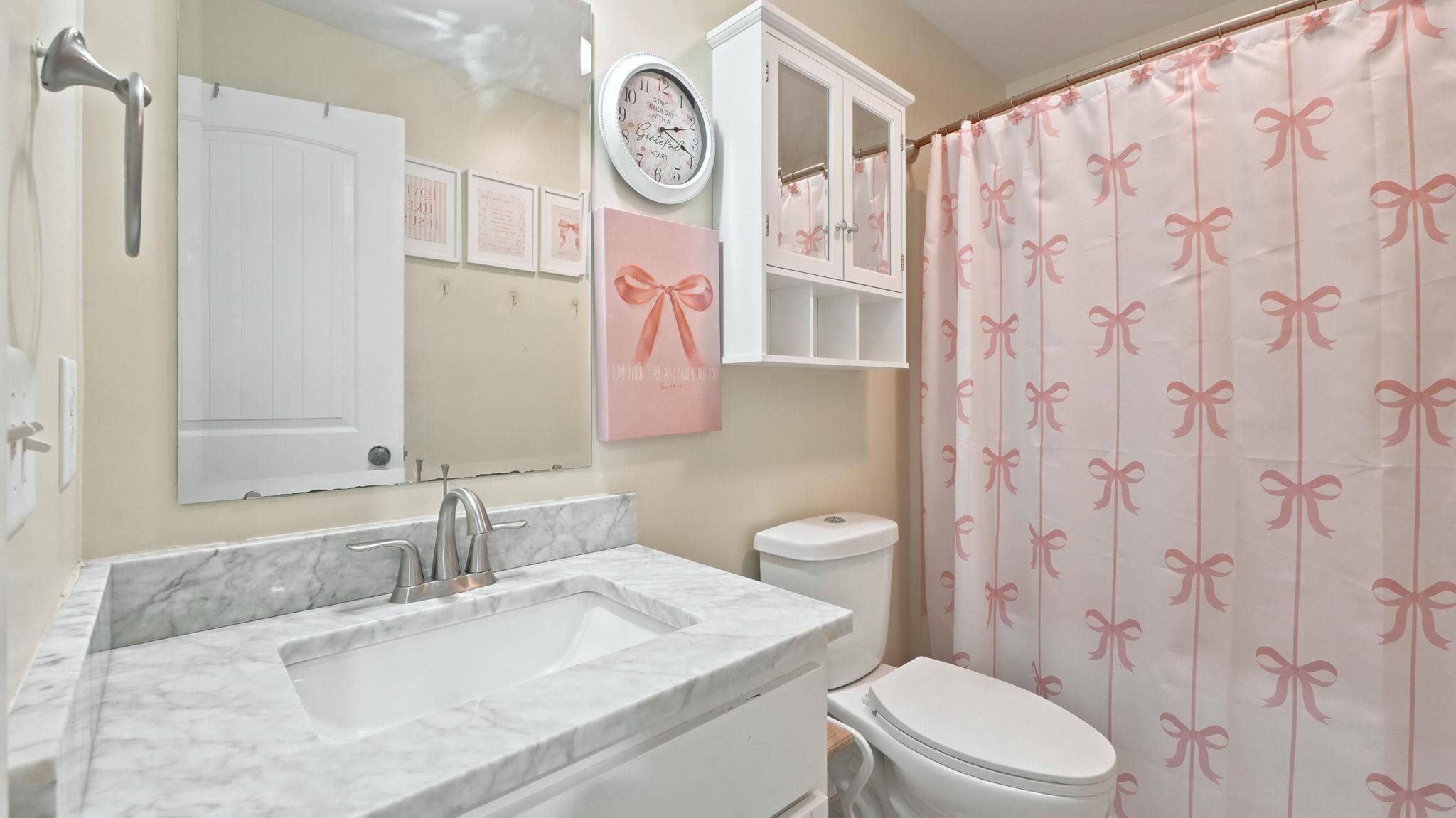 Bathroom featuring a stone-finish vanity top with an undermount sink, brushed nickel faucet, wall-mounted mirror, and white cabinetry