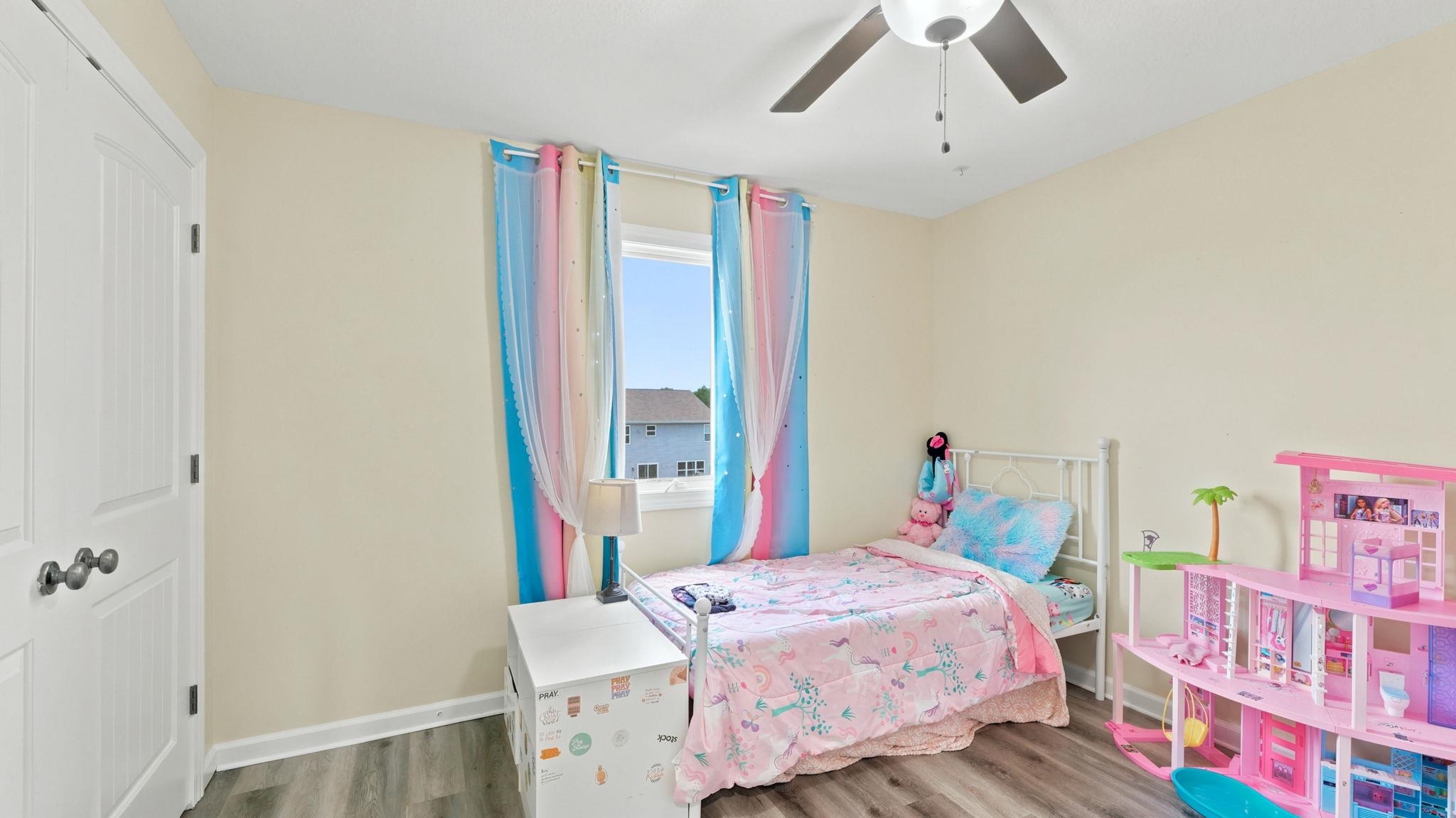 Room featuring wood-finish flooring, a white interior door with paneling, a double window, and a ceiling fan with integrated lighting