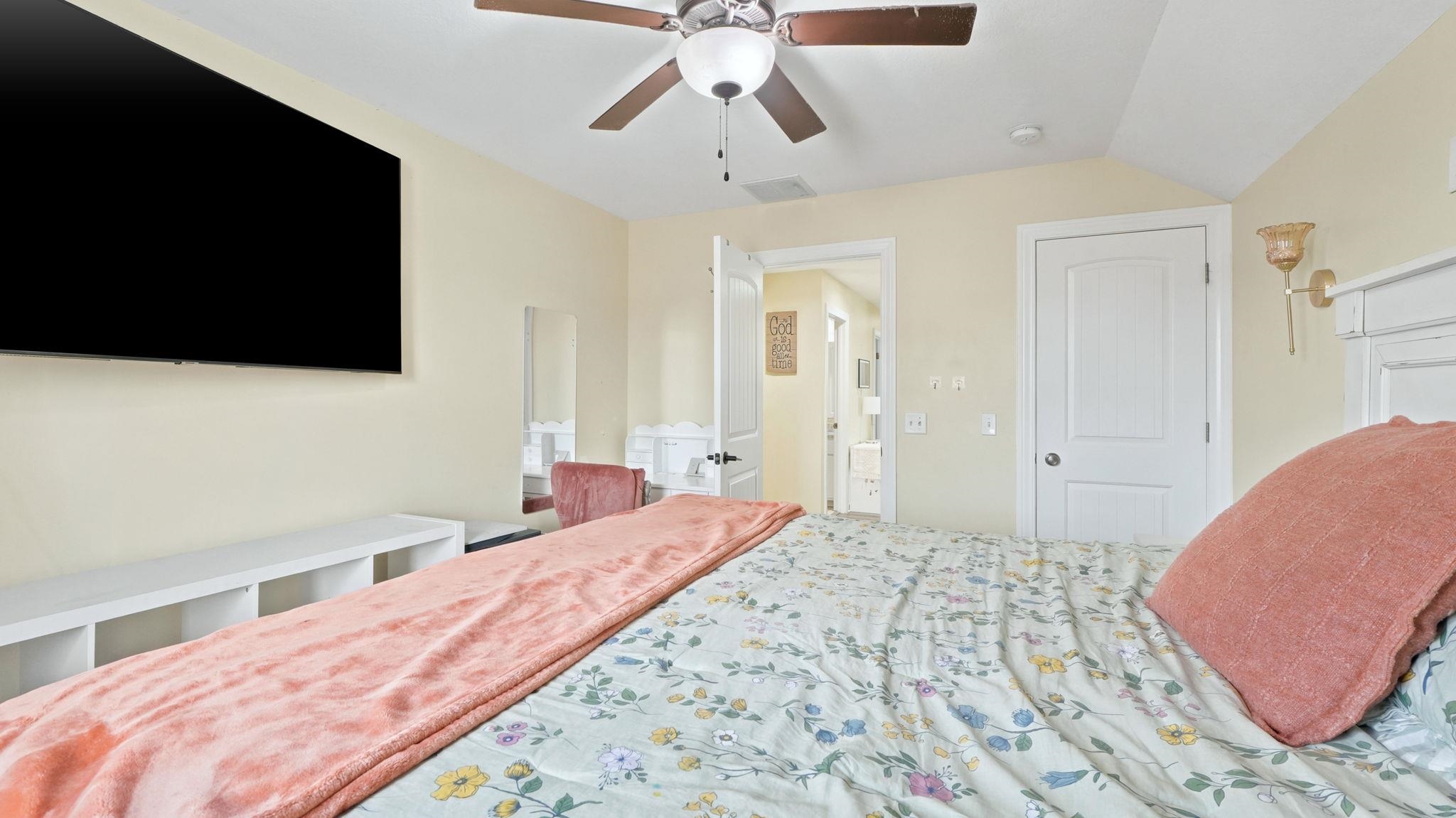 Bedroom featuring a ceiling fan with integrated lighting, a wall-mounted television, a built-in storage unit, and a paneled door
