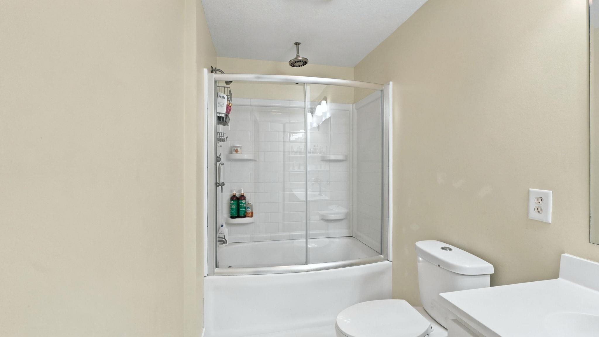 Bathroom featuring a white tub and shower combination with glass enclosure, white commode, and a white vanity with integrated sink