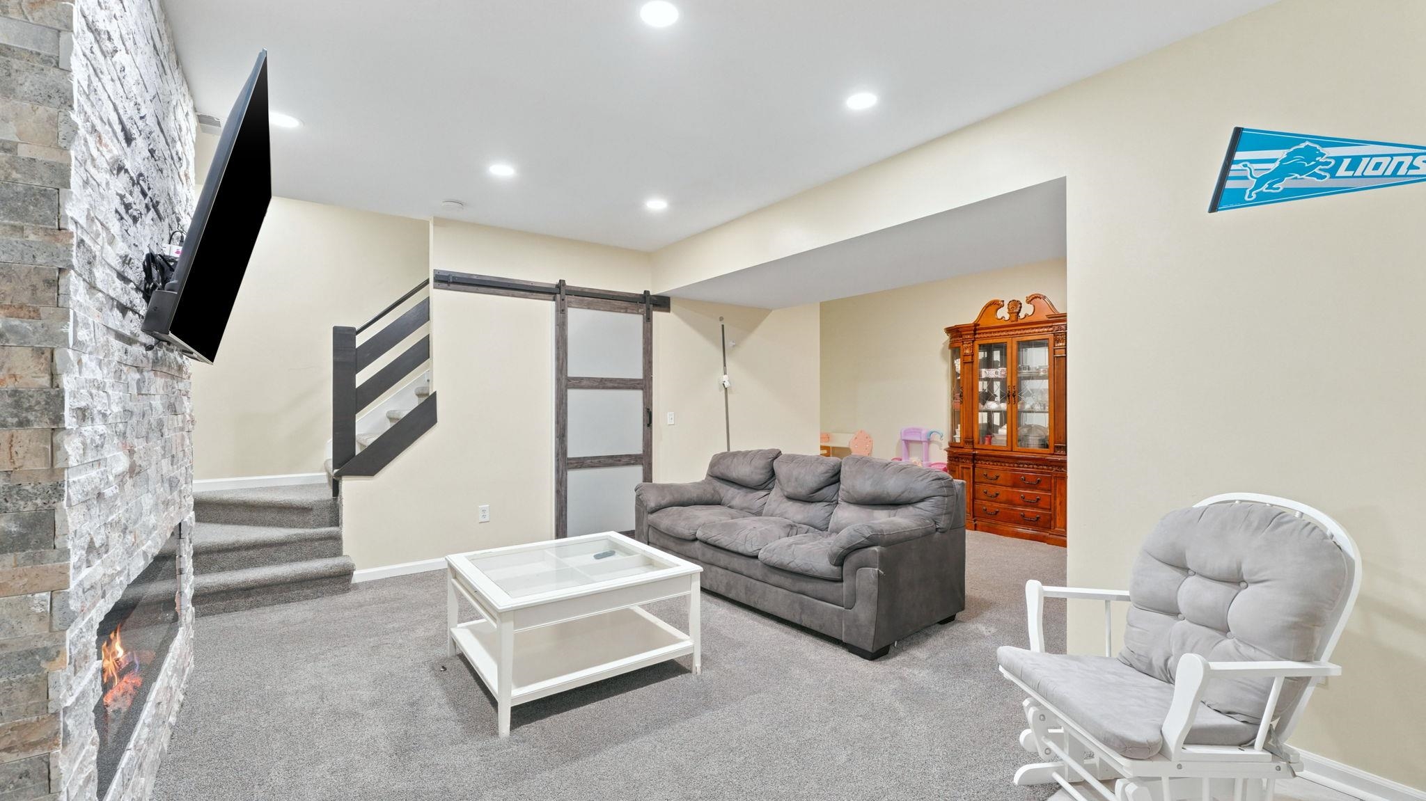 Finished living space featuring a stone veneer accent wall with an integrated electric fireplace, recessed lighting, and soft gray carpeting