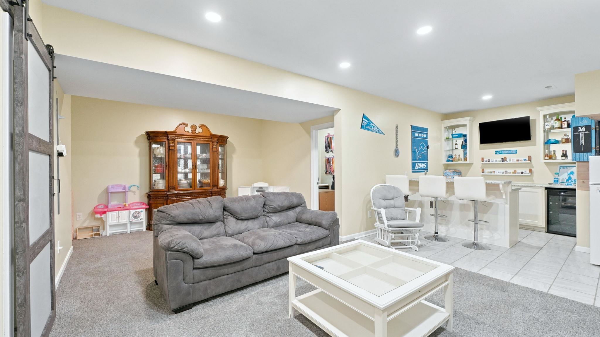 Spacious lower level featuring plush carpeting, recessed lighting, a built-in wet bar with tiled flooring, a beverage refrigerator, and an open entryway