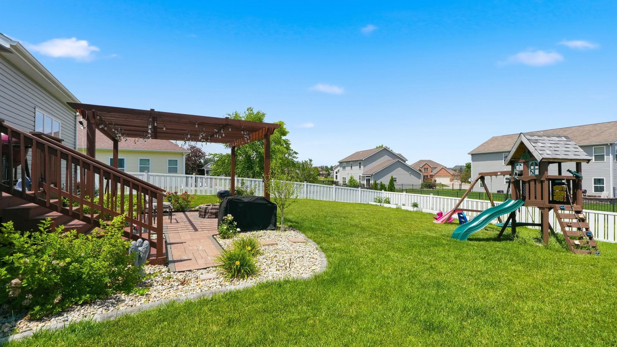 Expansive backyard featuring a manicured lawn, a white picket fence, and a wooden deck with a pergola-covered brick paver patio