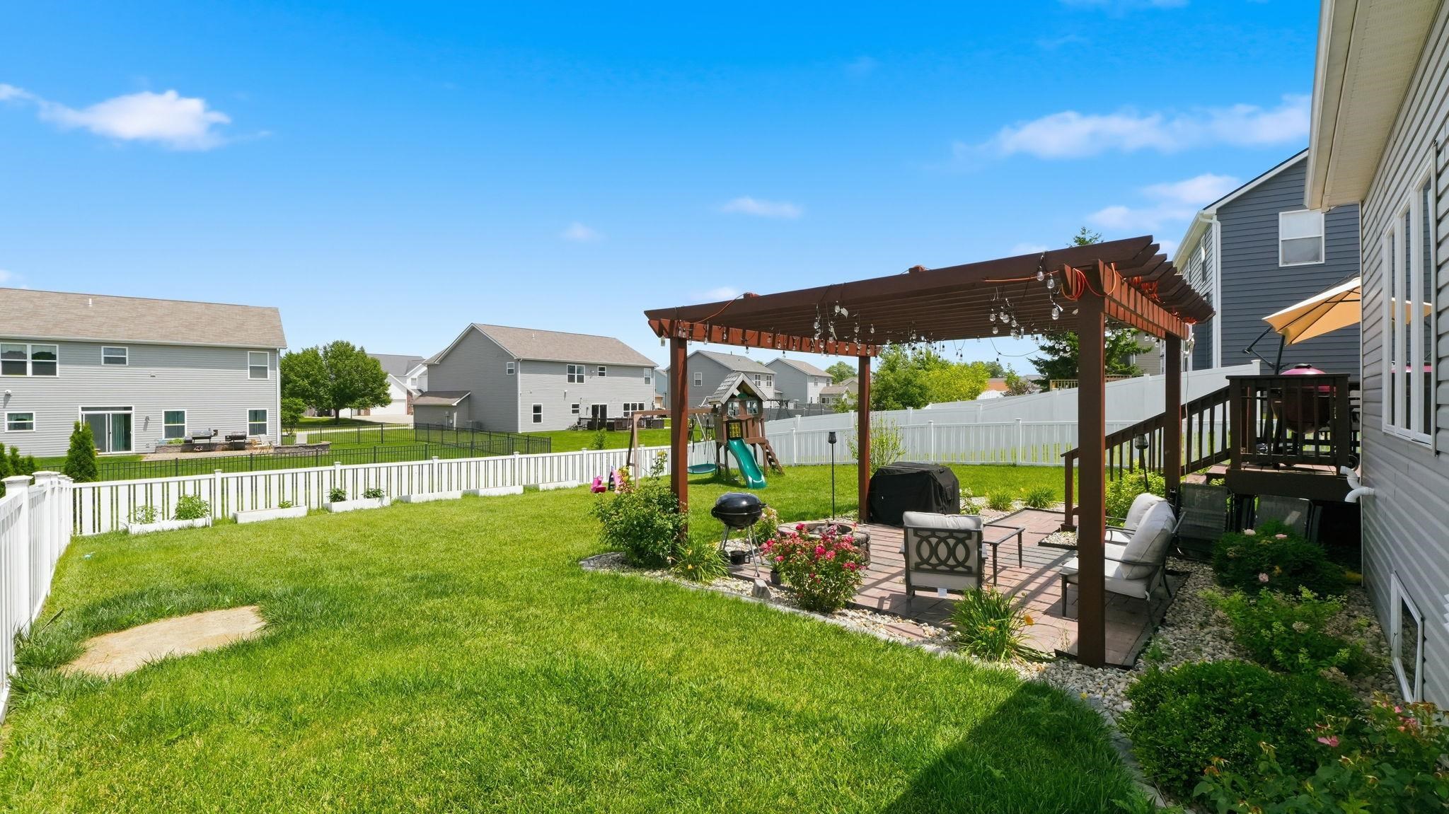 Expansive green lawn featuring a paver patio with a pergola, a multi-level deck, white picket fencing, and mature landscaping