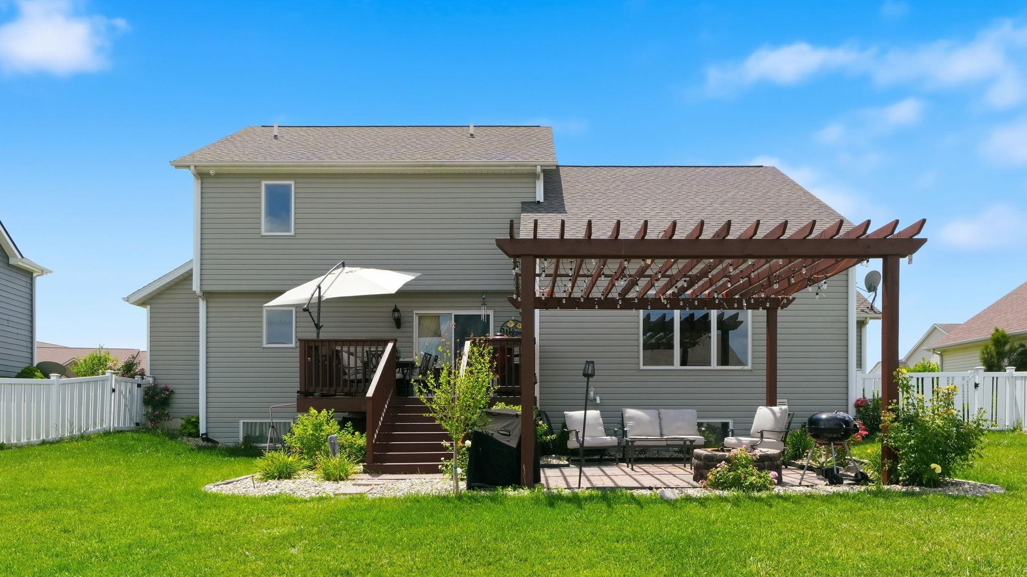 Expansive backyard featuring a manicured lawn, a two-story wood-finish deck with stairs, a stone patio, and a large wood-finish pergola