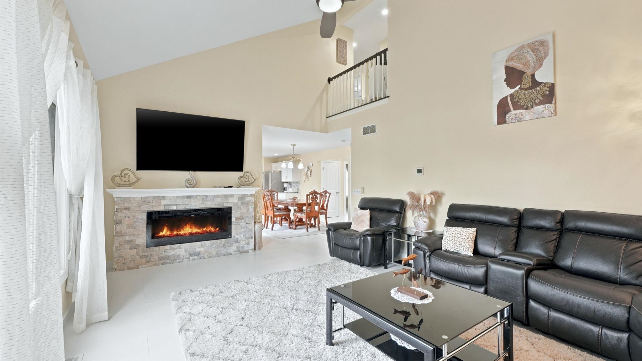 Spacious living area featuring a vaulted ceiling and an electric fireplace with a stone surround