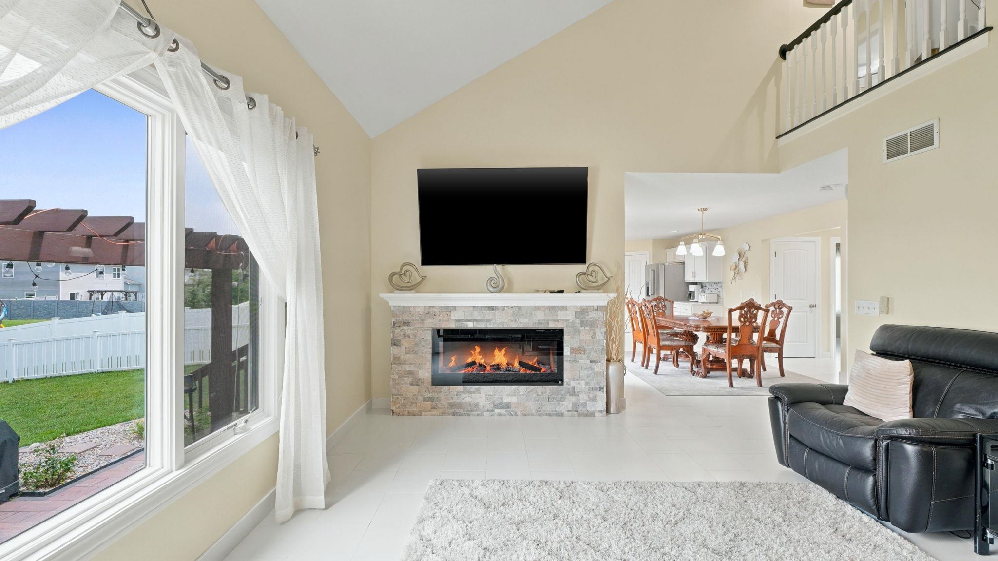 Living area with vaulted ceilings, a stacked stone fireplace with mantle, and a large picture window overlooking the backyard