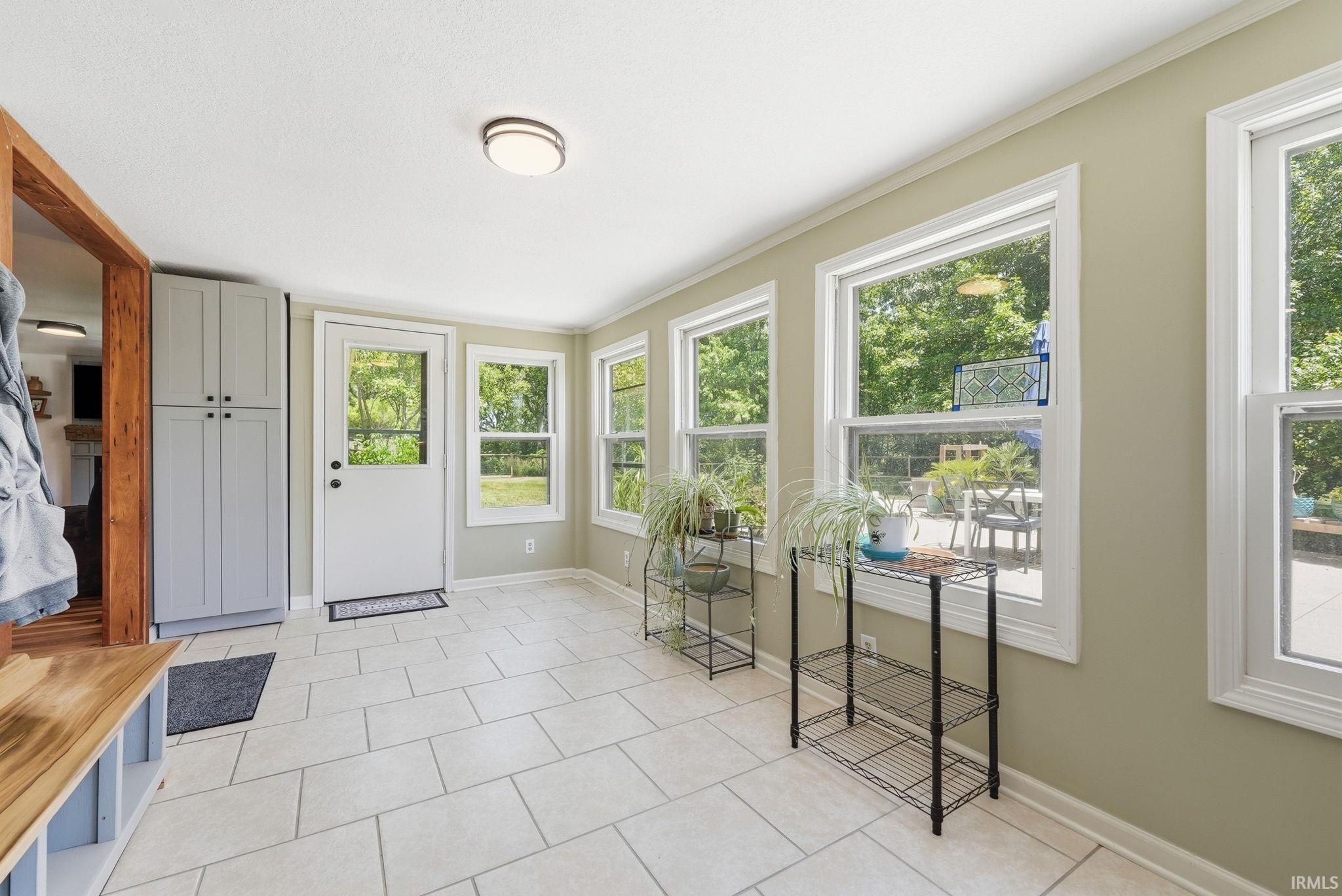 Light-filled room featuring large tile flooring, multiple windows, a full-light exterior door, and built-in cabinetry
