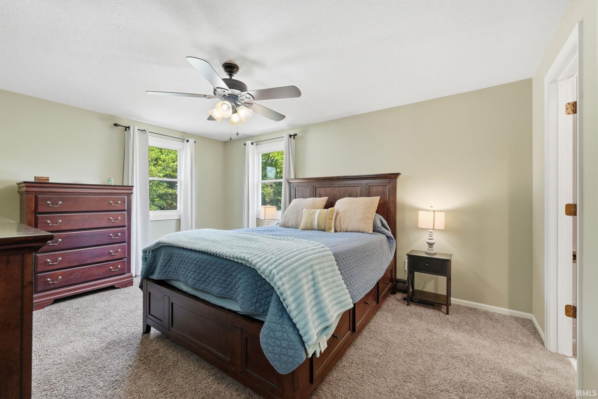 Carpeted room featuring a ceiling fan with integrated lighting, two windows, and a light-colored wall finish