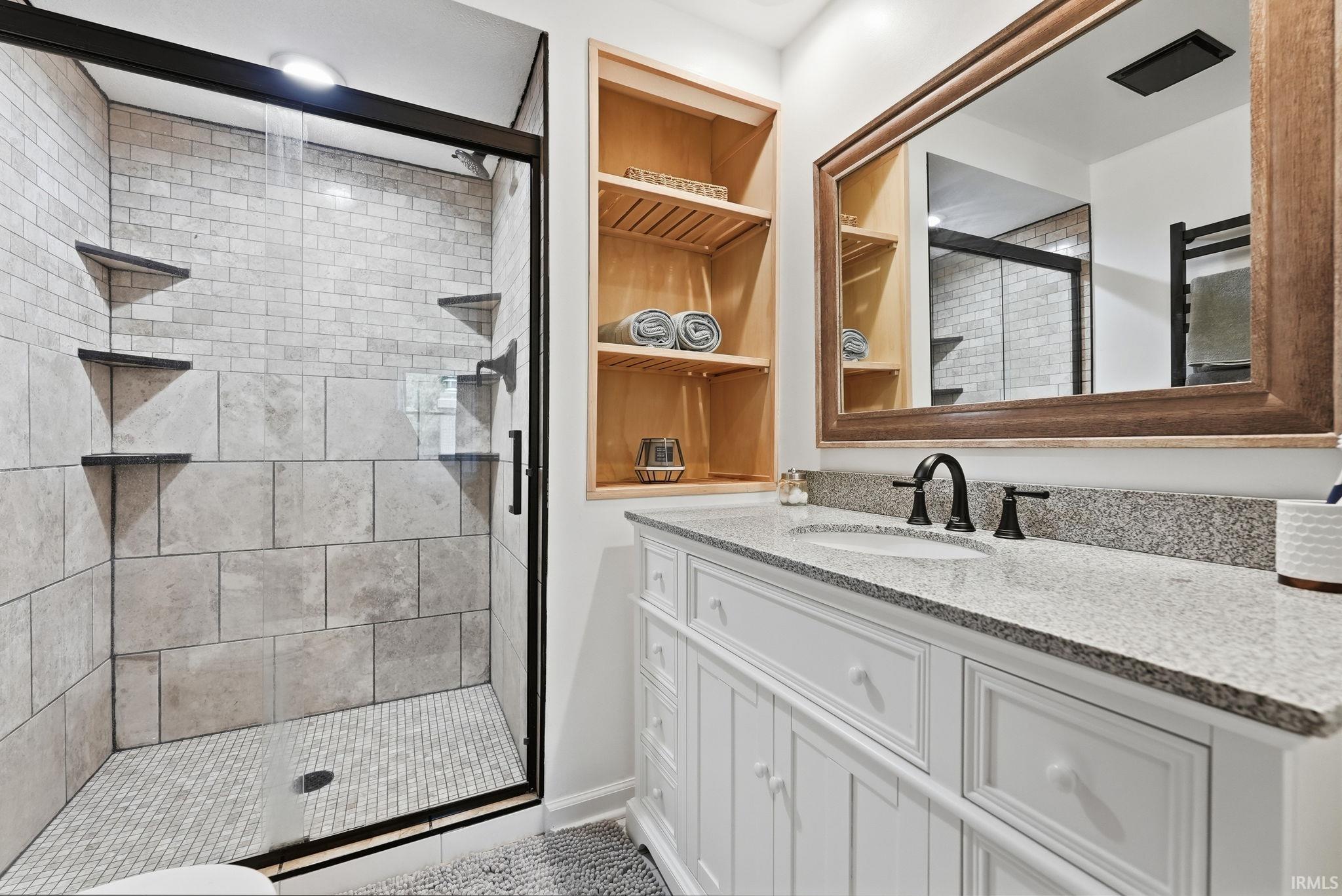 Full bathroom featuring a frameless glass shower enclosure with subway tile and integrated shelving