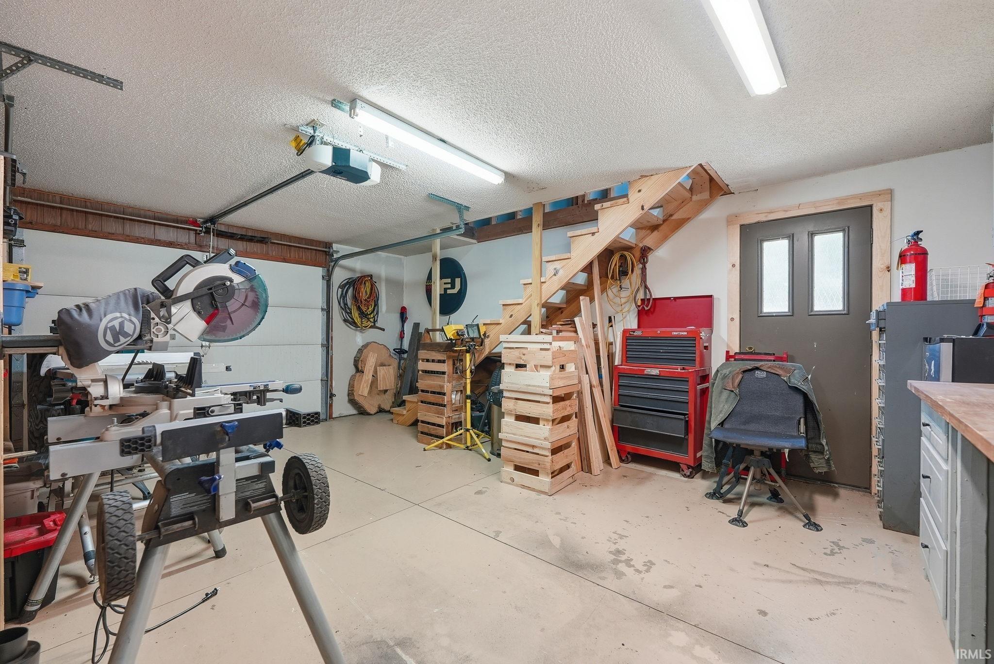 3rd bay of garage featuring a concrete floor, overhead fluorescent lighting, an insulated garage door, and a built-in wooden staircase leading to attic storage