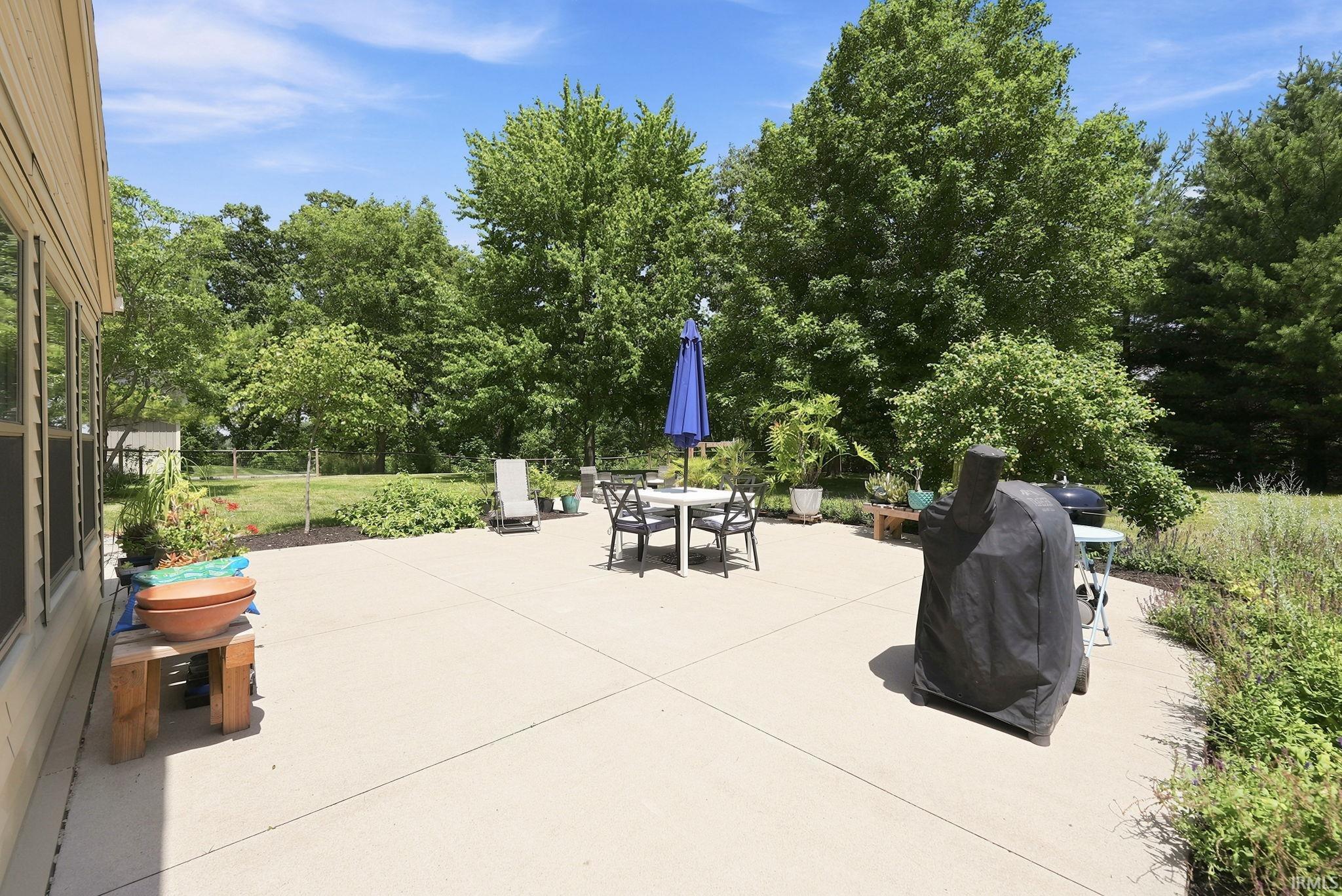 Expansive concrete patio with generous proportions, surrounded by mature trees and lush landscaping