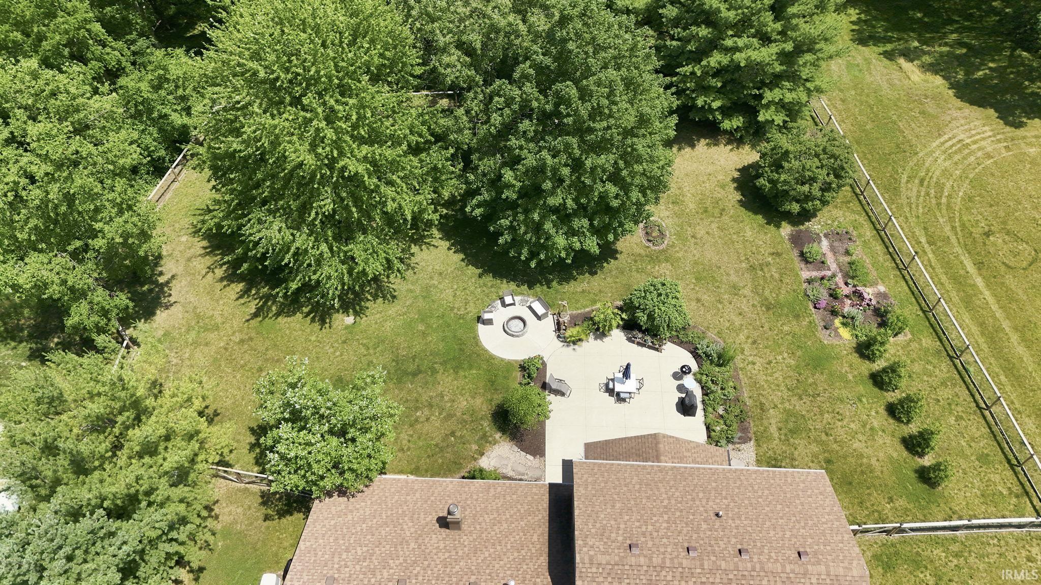 Expansive backyard featuring a stone patio, circular stone fire pit area, garden beds, and mature trees