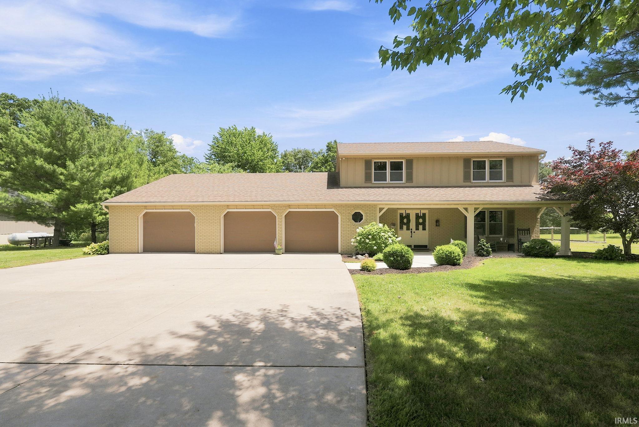 Two-story home featuring a covered front porch with white columns, a three-car garage, and a concrete driveway