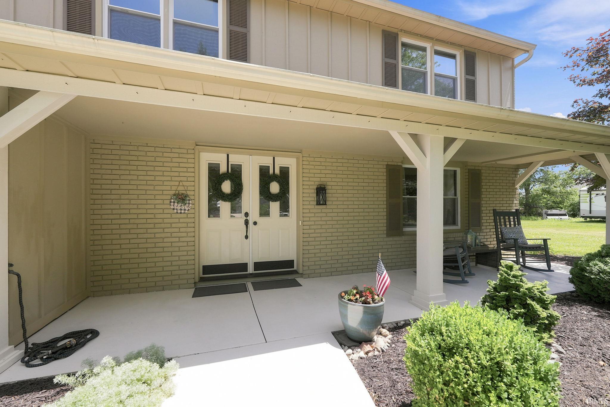 Covered front porch featuring a double entry door with glass inserts, brick facade, and decorative shutters