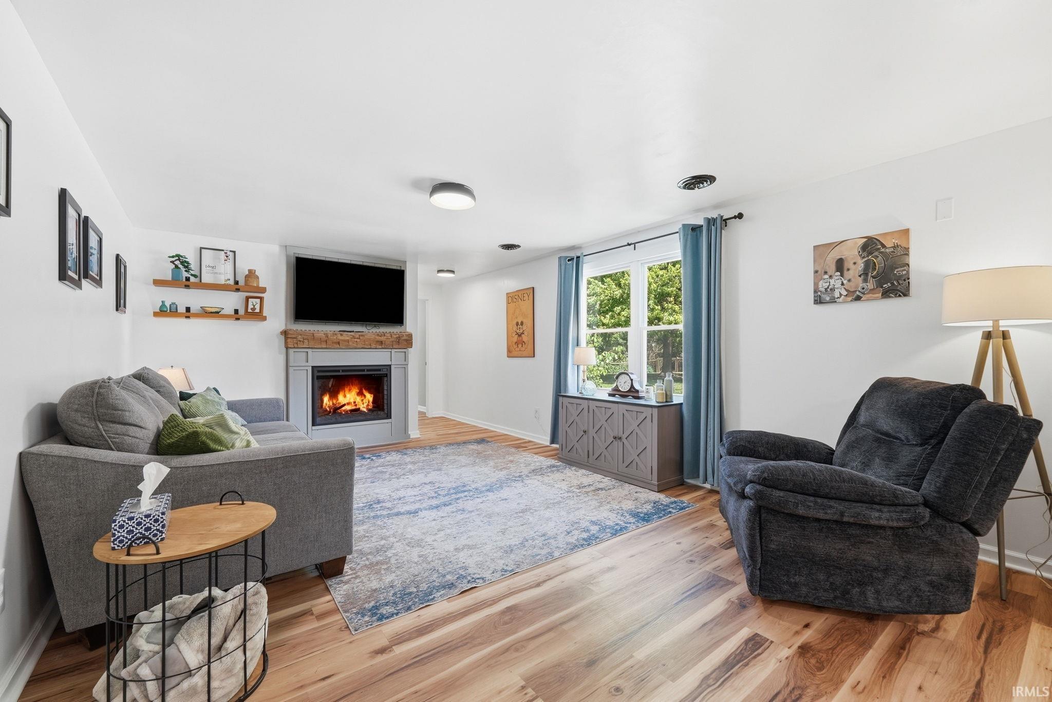 Living area featuring wood-finish flooring, a corner fireplace with a wood mantel, and built-in shelving