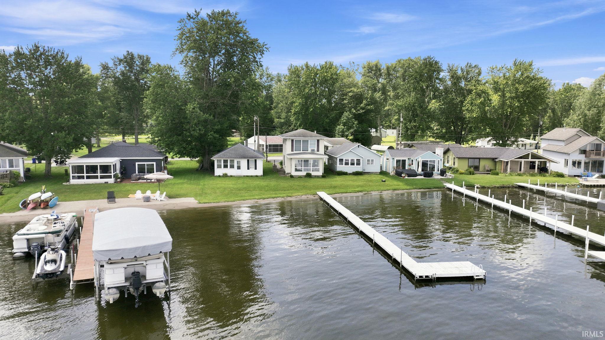 Waterfront property featuring an expansive lawn, mature trees, and a private boat dock with an attached lift