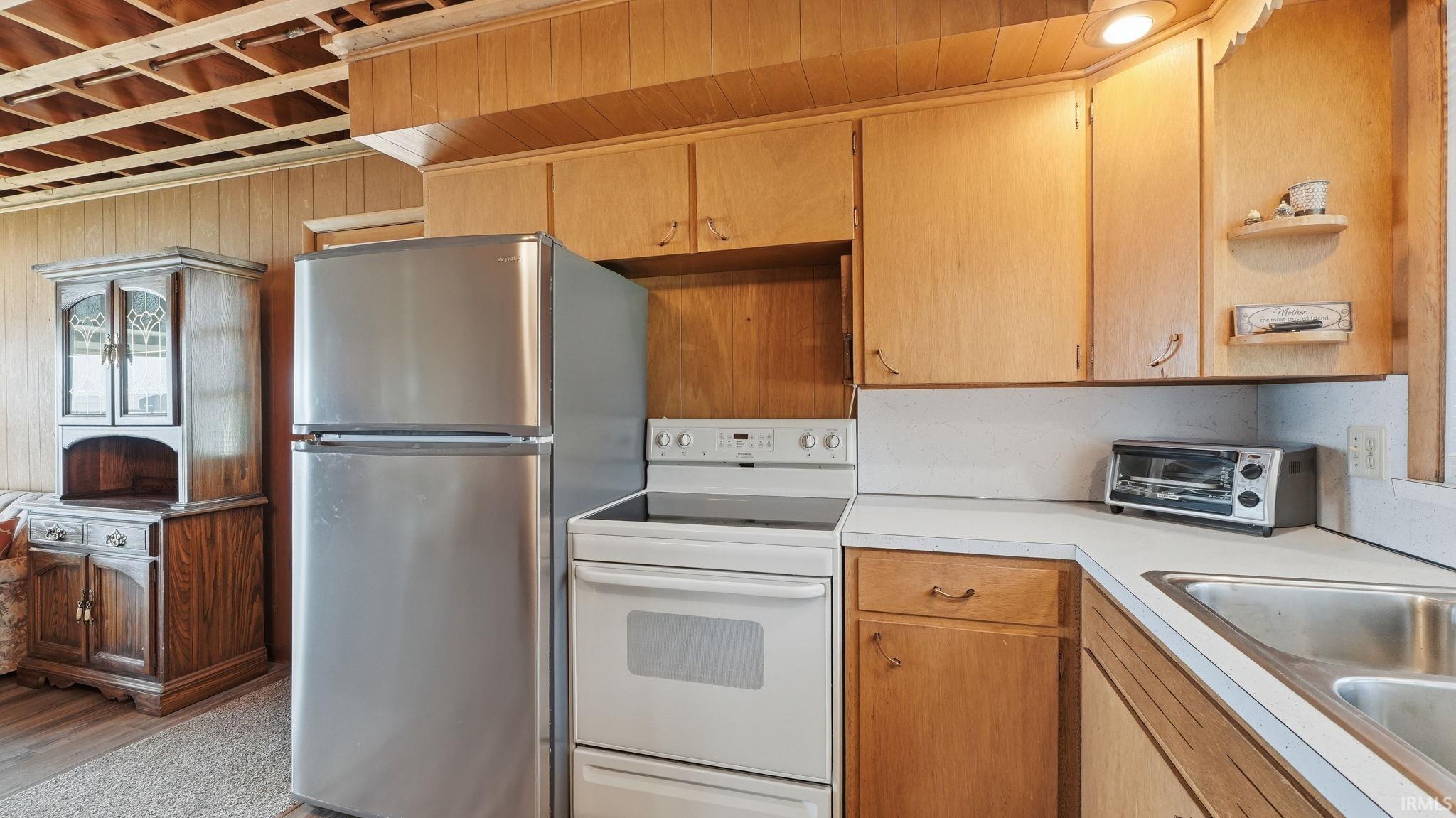 Kitchenette featuring wood-paneled walls, light wood cabinetry, white countertops, and a stainless steel refrigerator