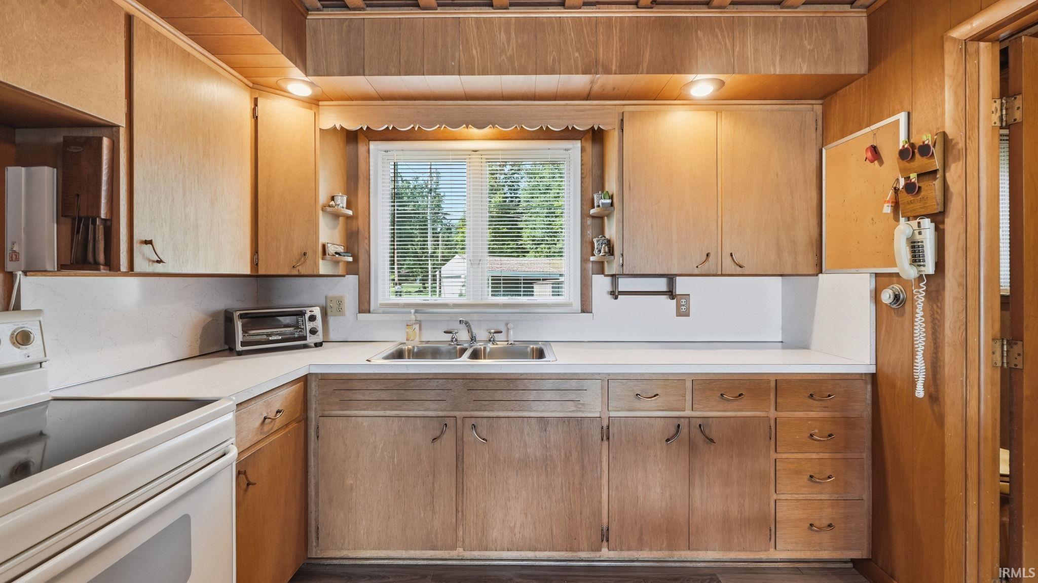 Kitchen featuring wood-panel walls and ceiling, light-toned cabinetry, white countertops, a double basin sink, and a built-in electric range
