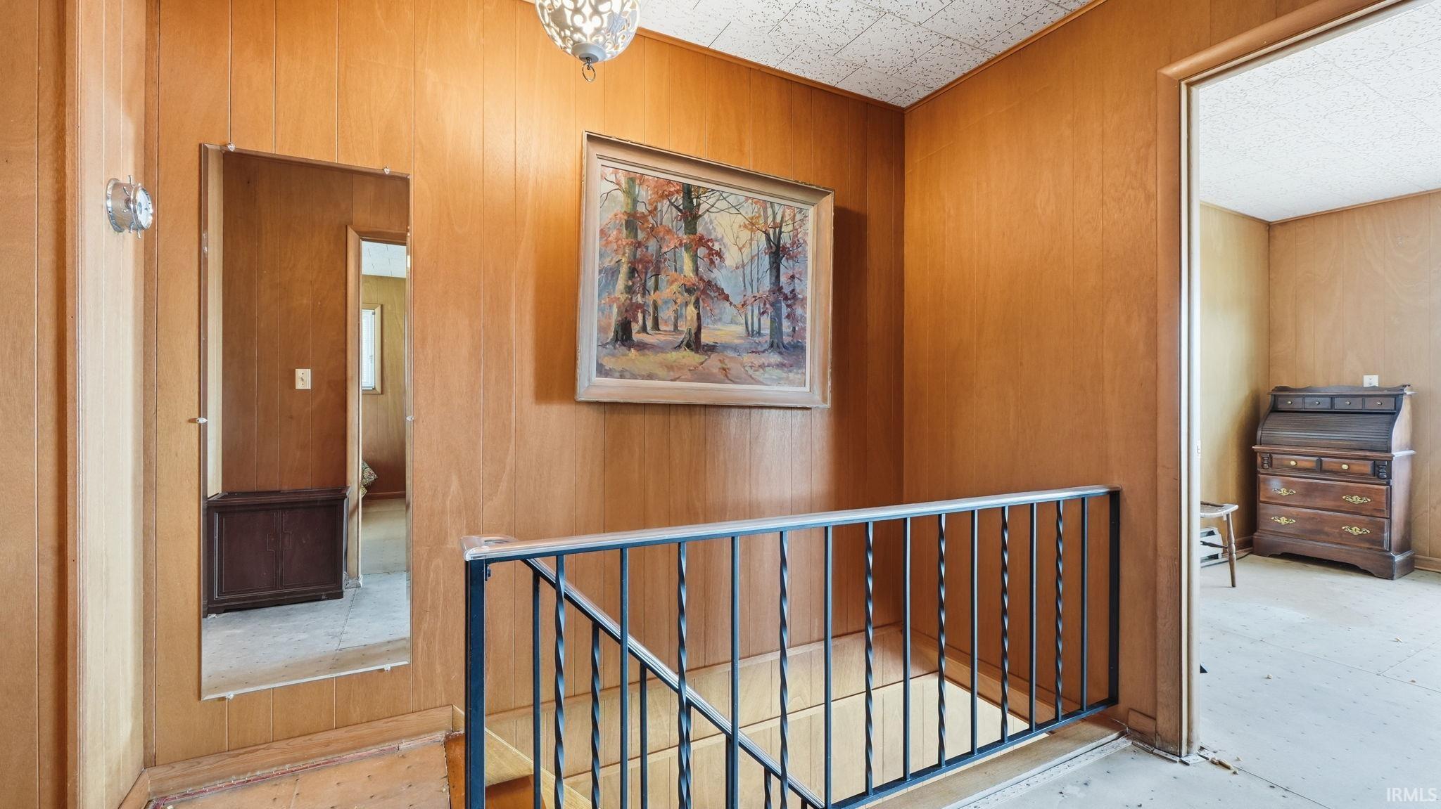 Wood-paneled hallway with textured ceiling and dark metal stair railing