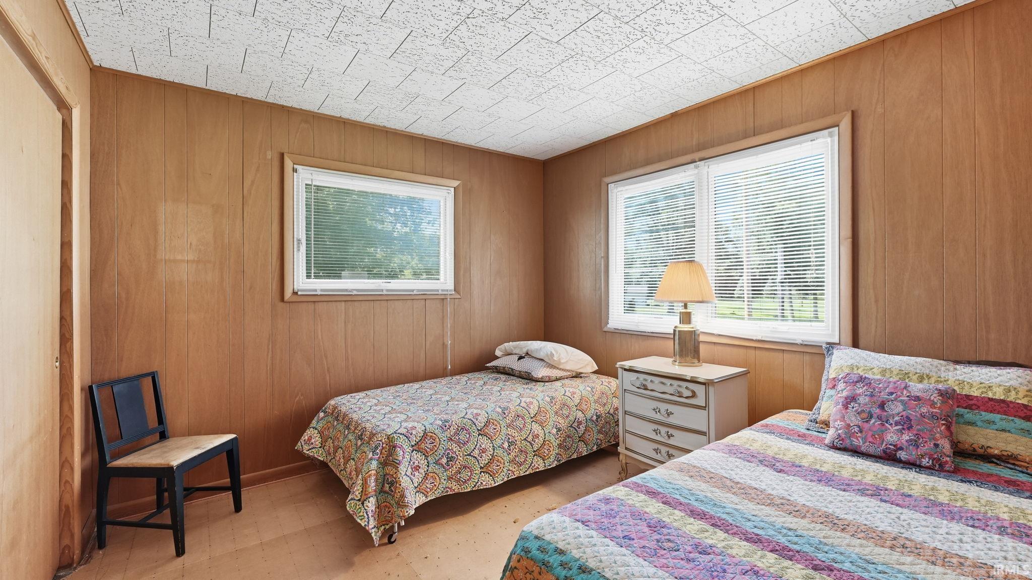 Room featuring wood panel walls, textured ceiling, and two windows with blinds