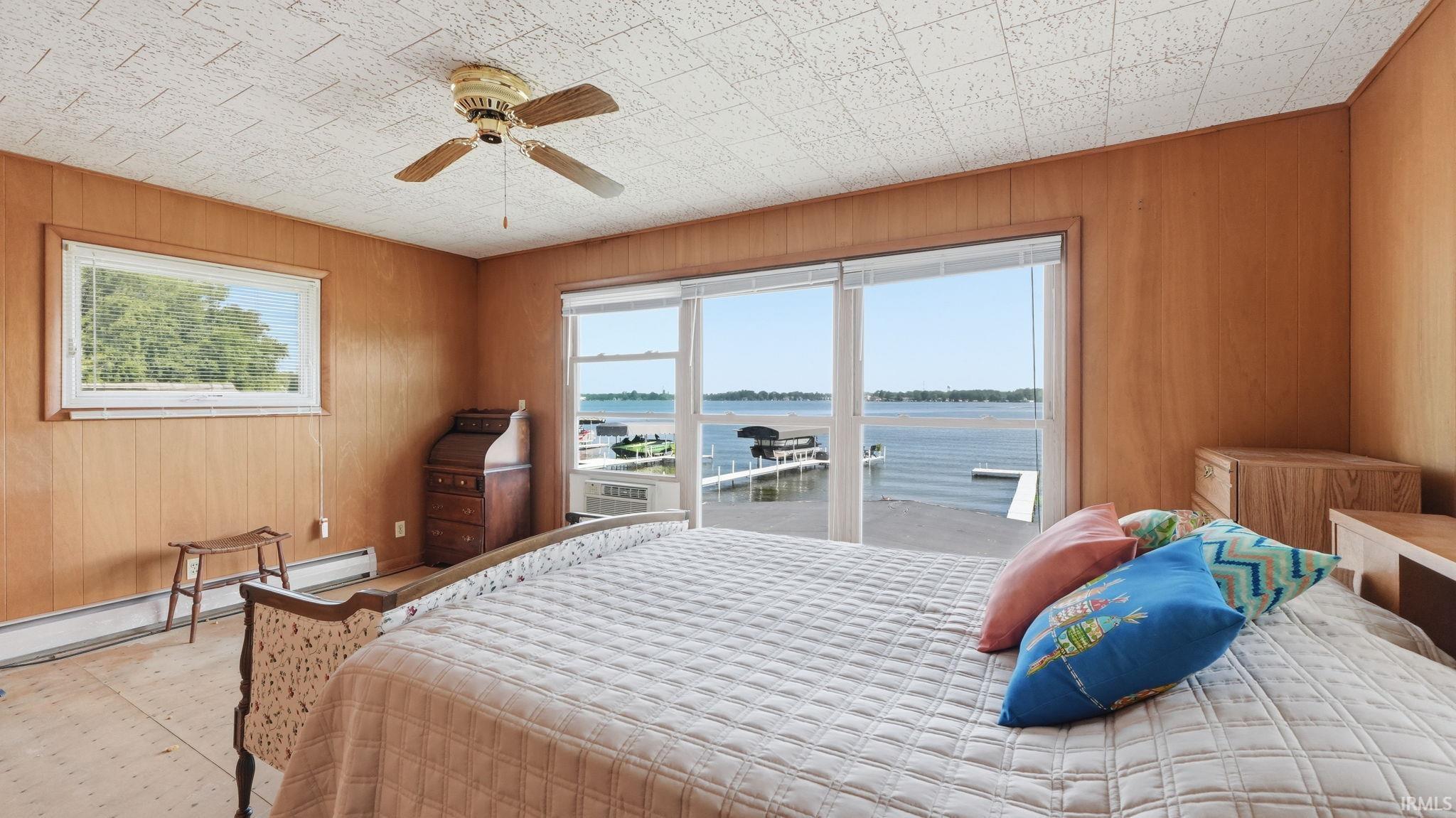 Room featuring expansive water frontage, panoramic water views, a ceiling fan, wood-paneled walls, and a large picture window