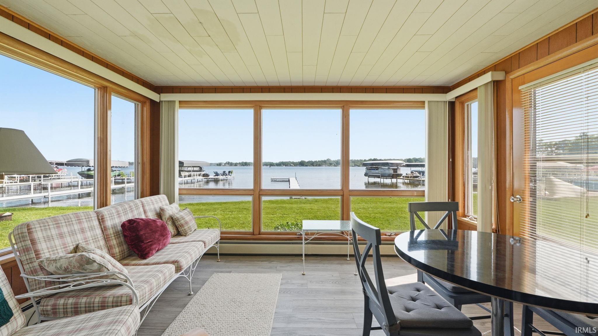 Sunroom featuring expansive windows with water frontage, wood-finish paneling, and a light-toned plank ceiling