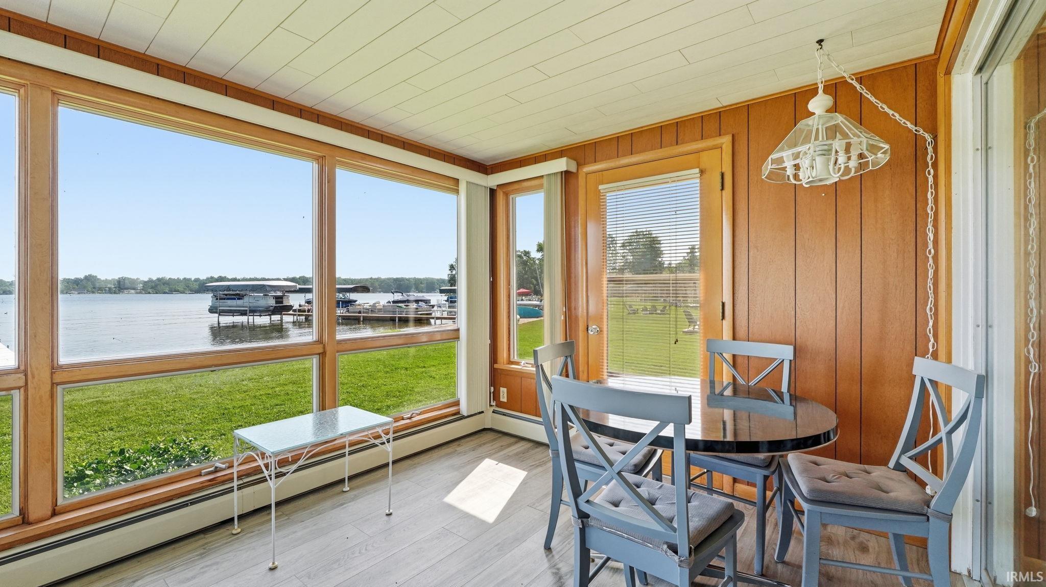 Sunroom featuring expansive lakefront windows, wood-finish paneling, a paneled ceiling, and wood-finish flooring
