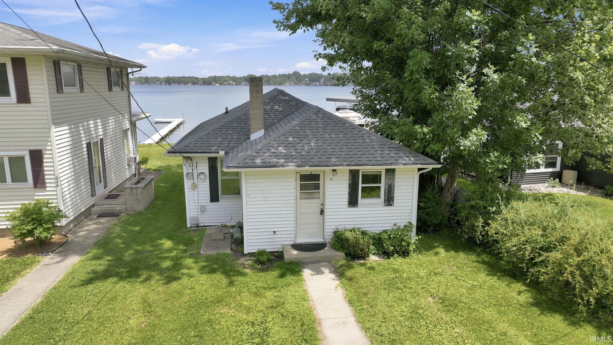 Waterfront property featuring a white siding exterior, dark shingled roof, a chimney, and a front pathway
