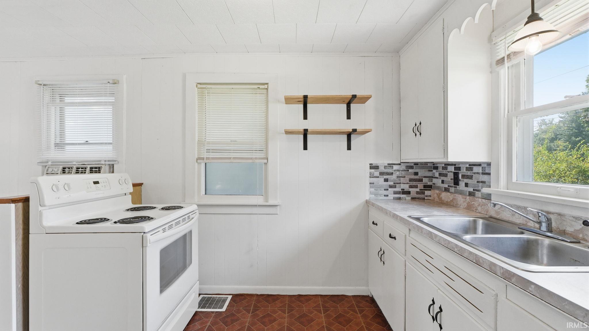 Kitchen featuring white cabinetry with decorative hardware, a double basin sink, and a multi-tone tile backsplash