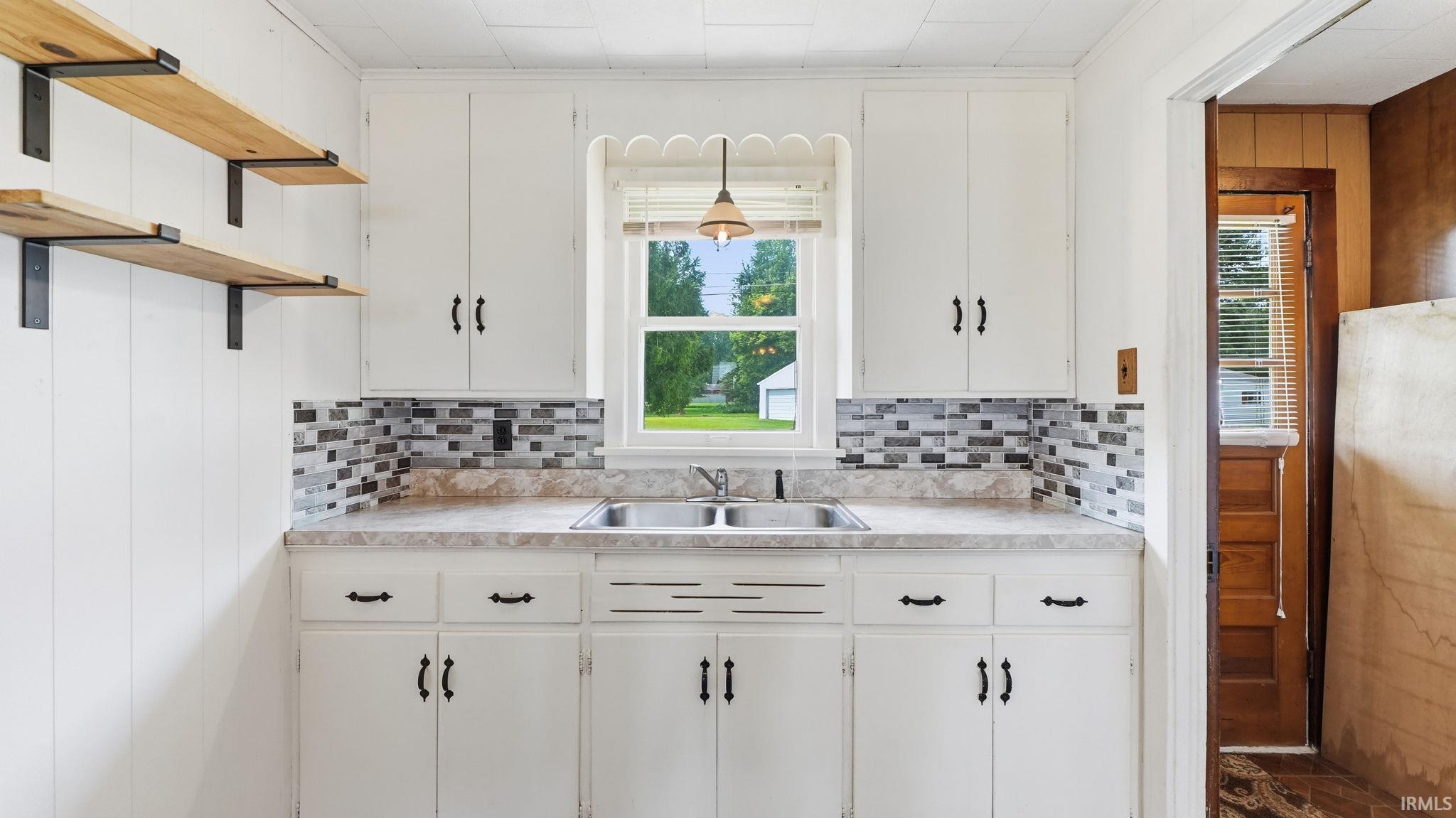 White cabinetry with black hardware, a mosaic tile backsplash, and a double basin sink beneath a window
