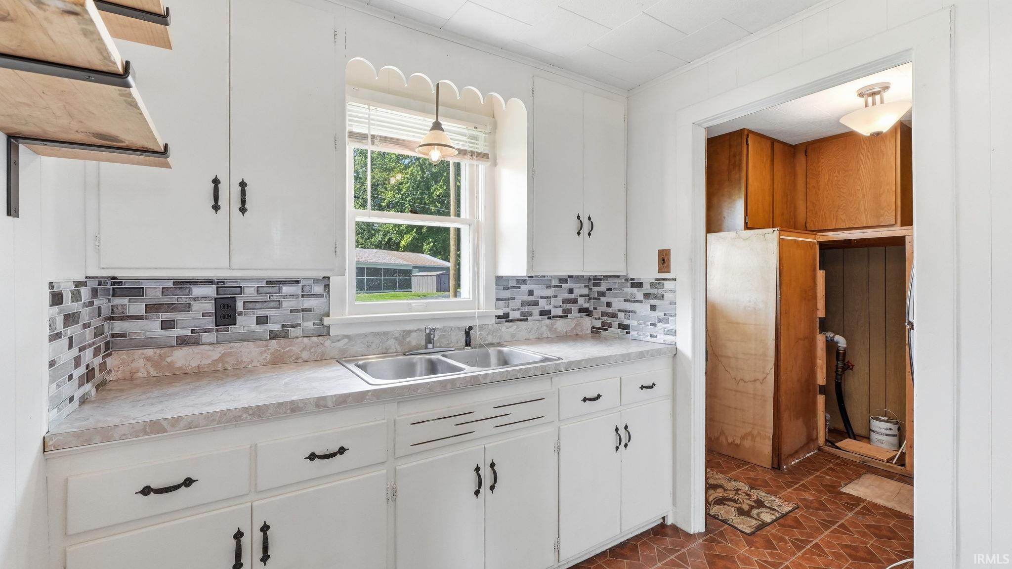Kitchen space featuring white cabinetry, a dual basin stainless steel sink, and a multi-tone tile backsplash