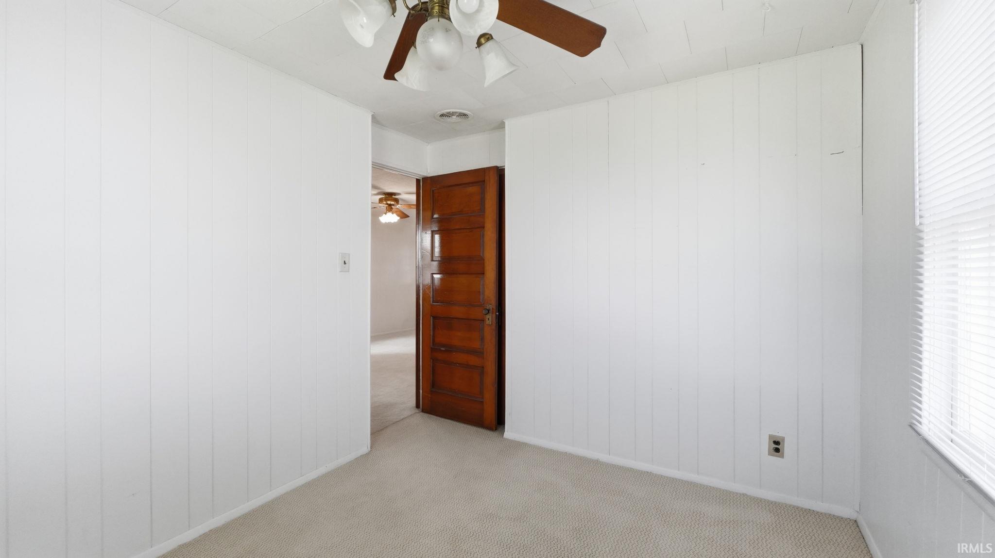 Carpeted room featuring vertical panel wall treatment, a window with horizontal blinds, and a brown wood panel door