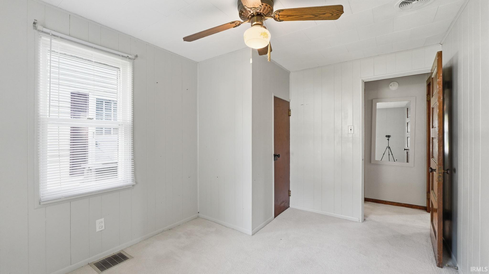 Room featuring light-colored carpet, a window with horizontal blinds, and paneled walls