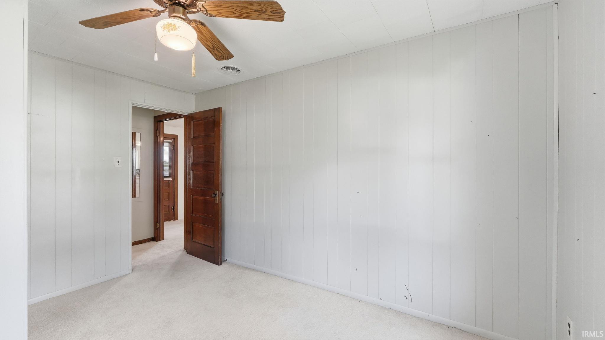 Room featuring light-colored carpeting, white vertical paneling, and an overhead ceiling fan with light fixture