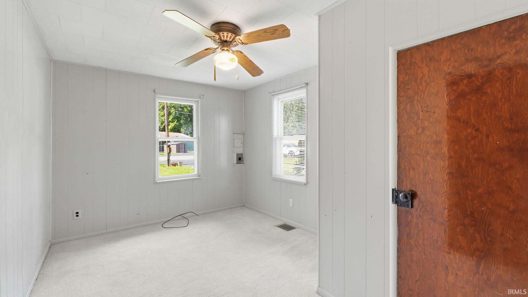 Light-filled room featuring white vertical paneling, two windows with white trim, and a ceiling fan with a central light fixture