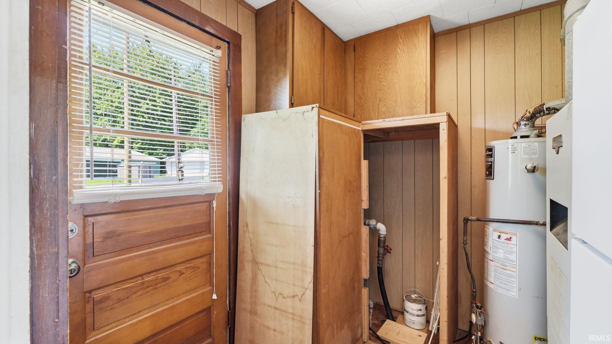 Wood-paneled room featuring a water heater, built-in cabinetry, and a door with an integrated window and blinds