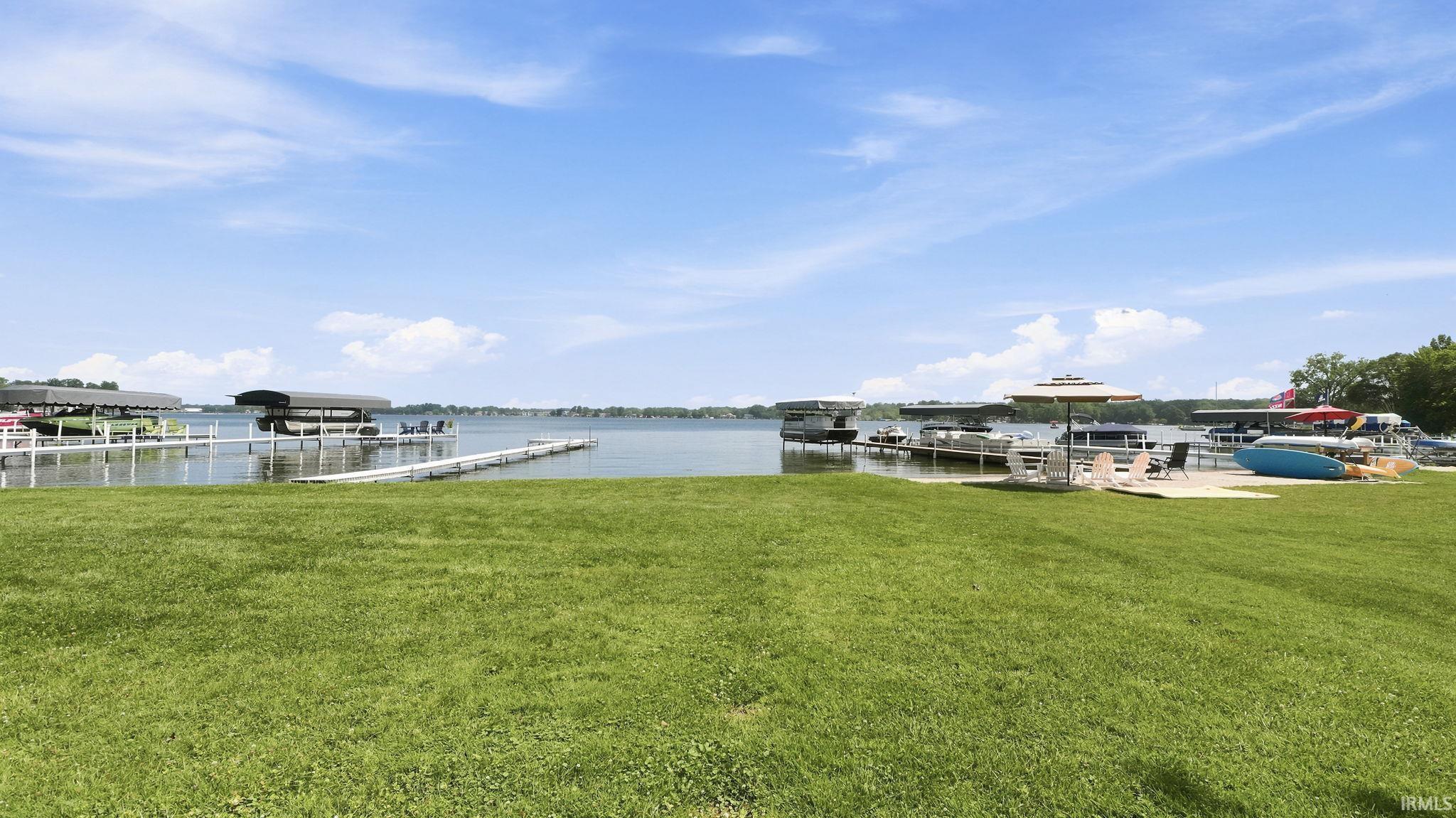 Expansive waterfront lawn featuring multiple boat docks with covered slips, direct water access, and a sandy beach area