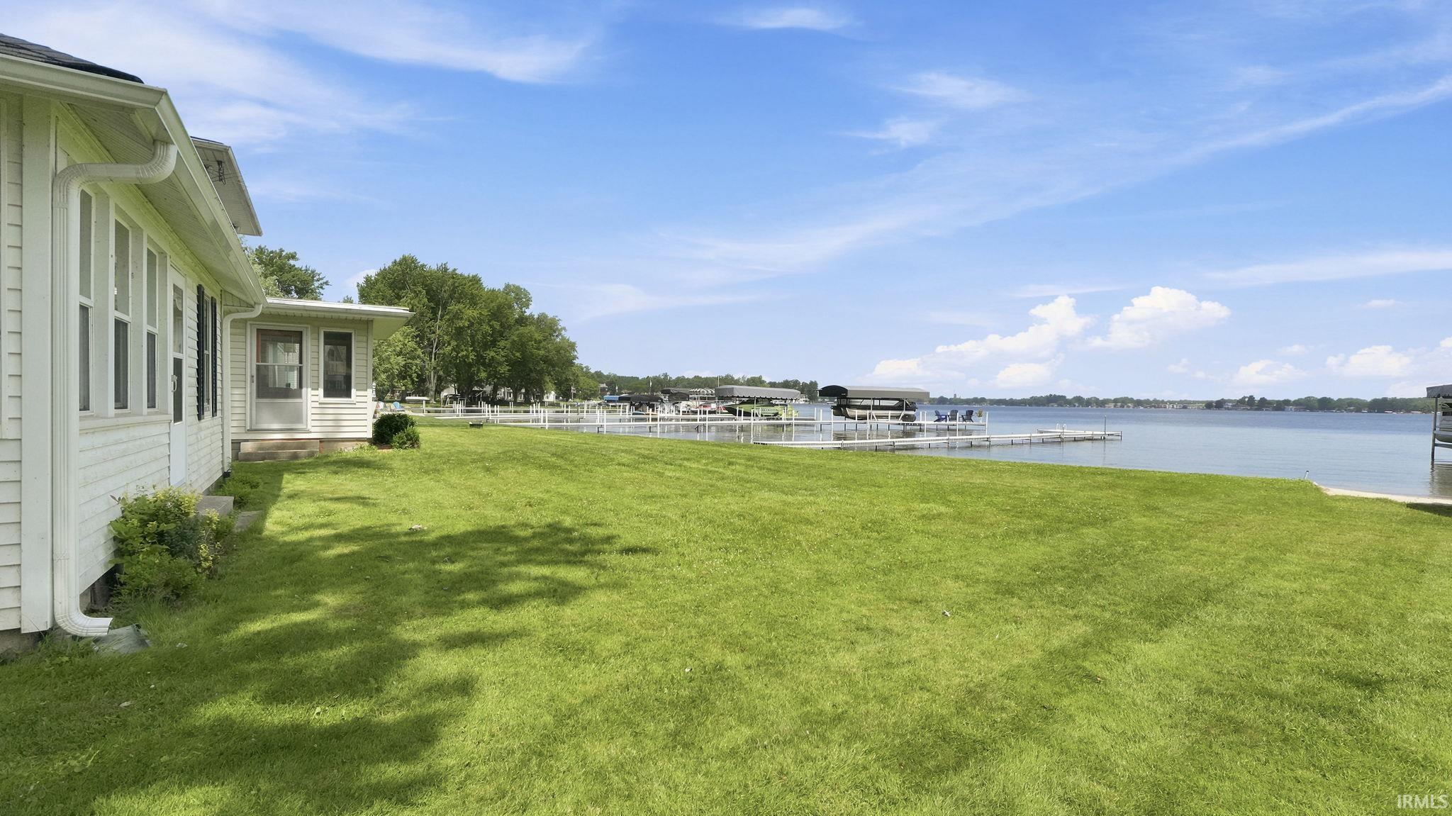 Expansive lakeside property featuring a manicured lawn, white siding, multiple windows, and a screened porch