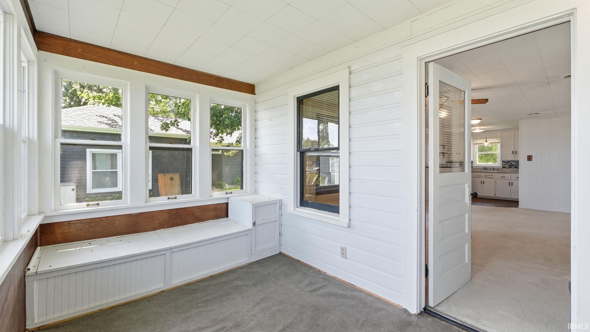 Sunroom featuring multiple windows, a built-in window bench with storage, shiplap-style wall paneling, and wood-finish trim