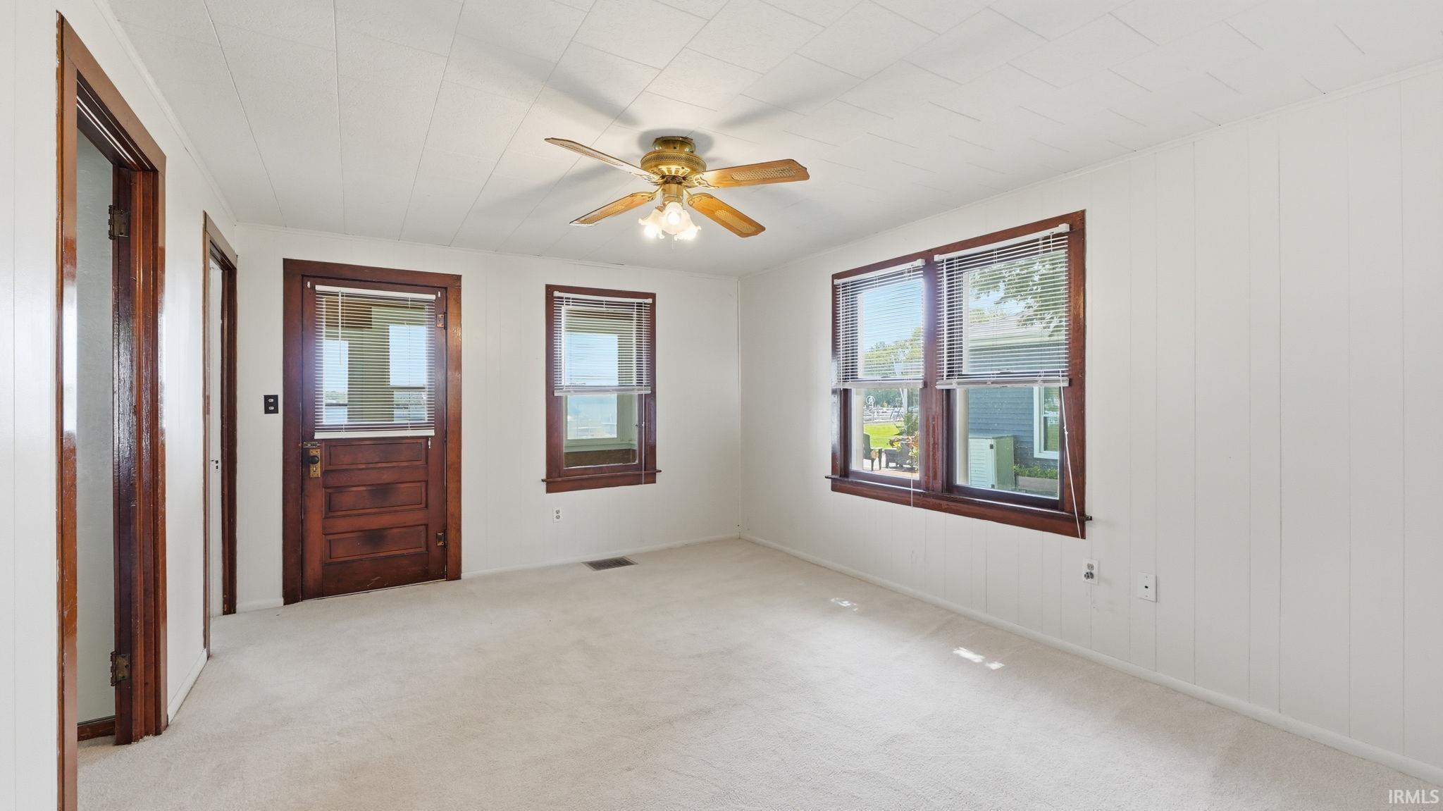 Carpeted room featuring white vertical paneling, dark wood trim around windows and doors, and a ceiling fan with light fixture