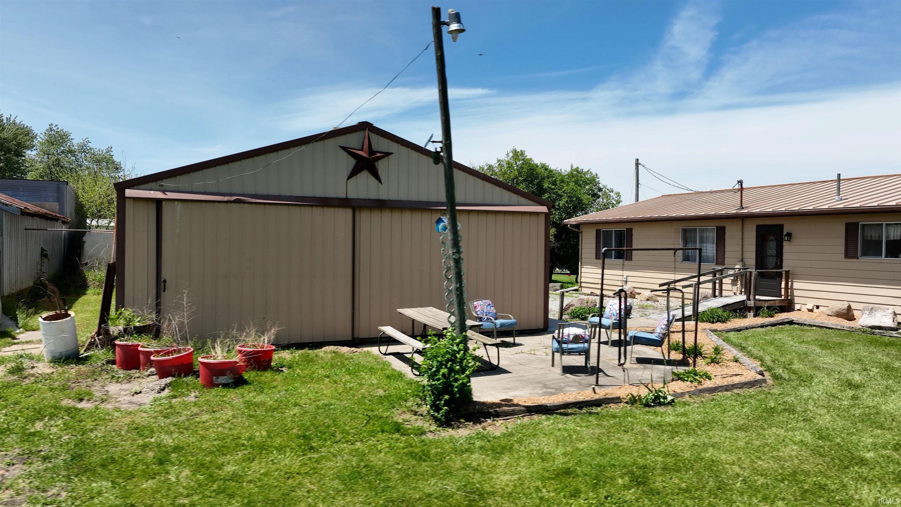 Expansive backyard featuring a large metal-sided shed with a gable roof, a concrete patio area, and a ramp leading to the residence