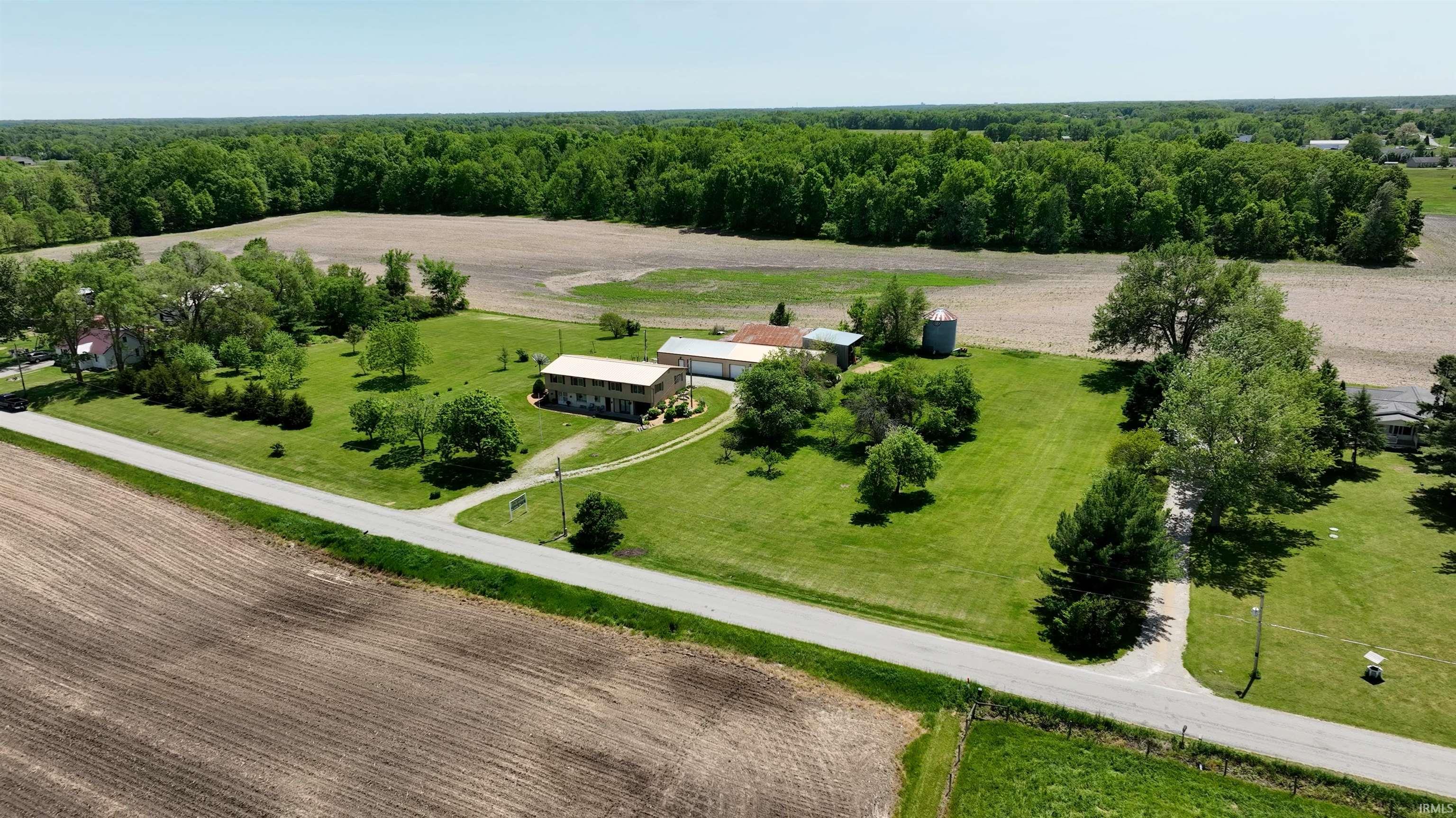 Expansive property featuring a two-story residence, detached outbuildings, a silo, and a large manicured lawn with mature trees