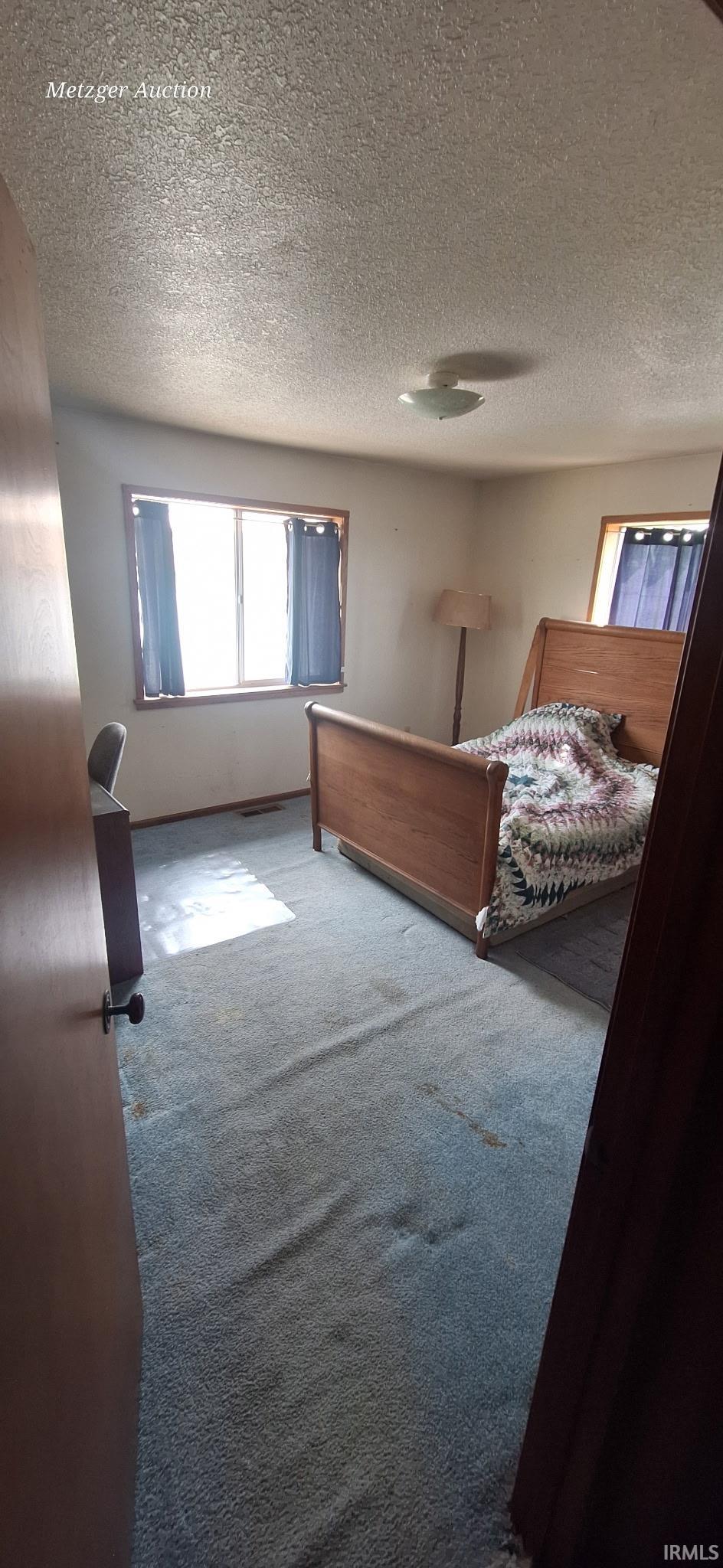 Carpeted interior space featuring two windows with curtain rods and privacy curtains