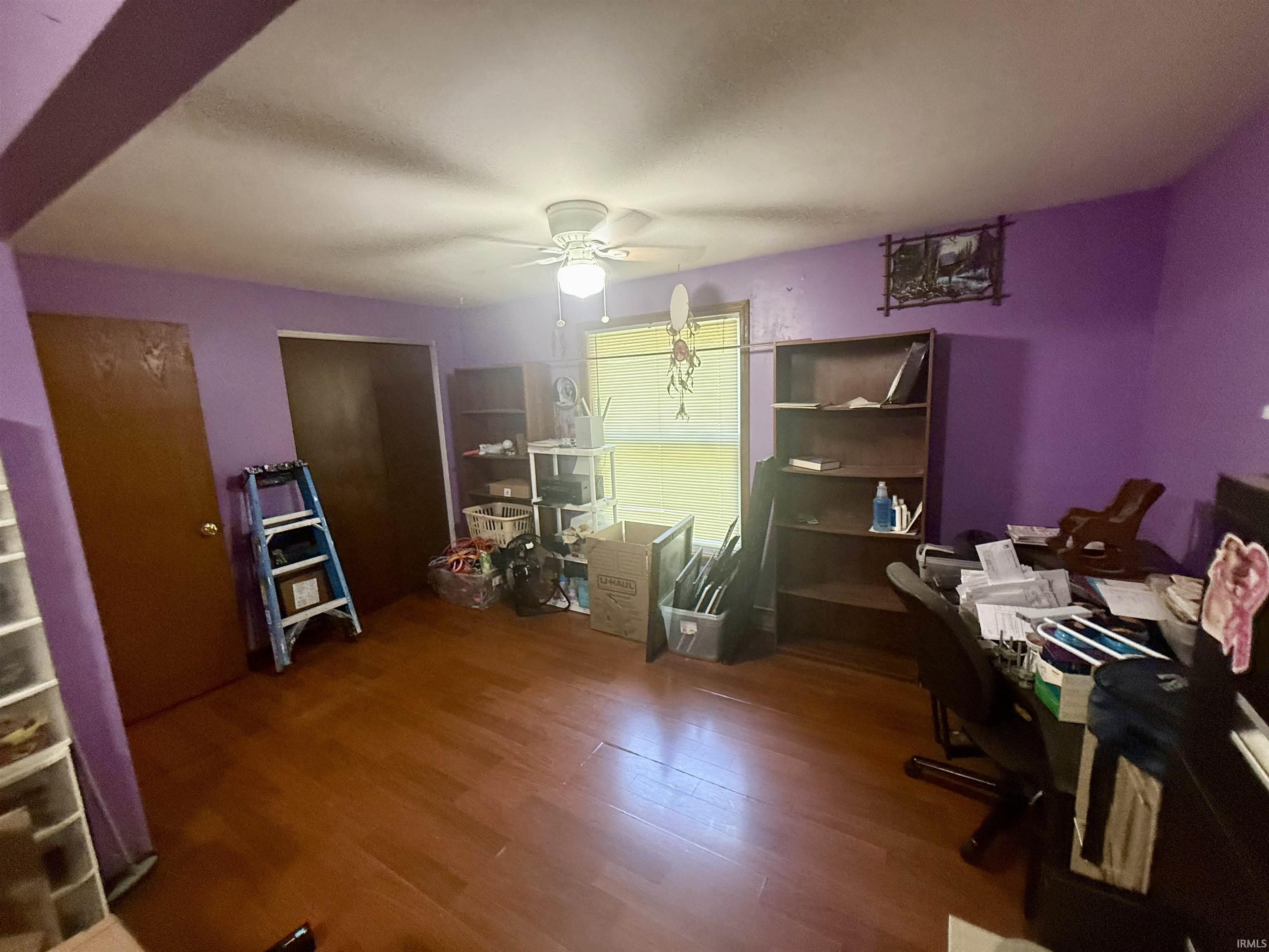 Room featuring wood-finish flooring, a ceiling fan with integrated lighting, and multiple built-in shelving units