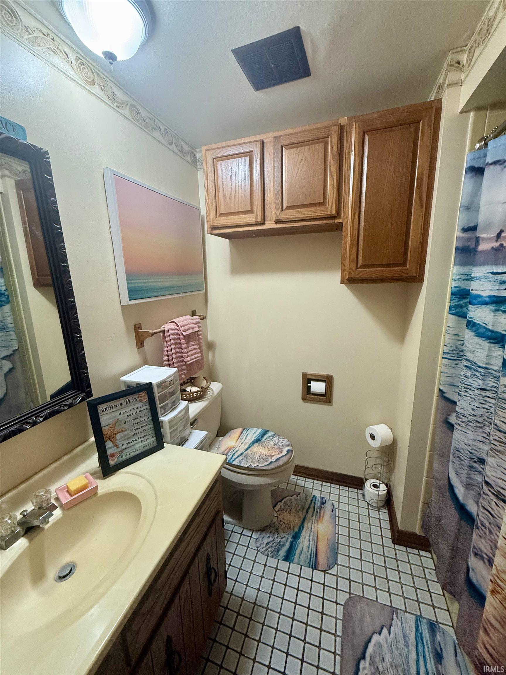 Bathroom featuring a single vanity with an integrated sink and light-toned countertop, a toilet, and overhead wood cabinetry