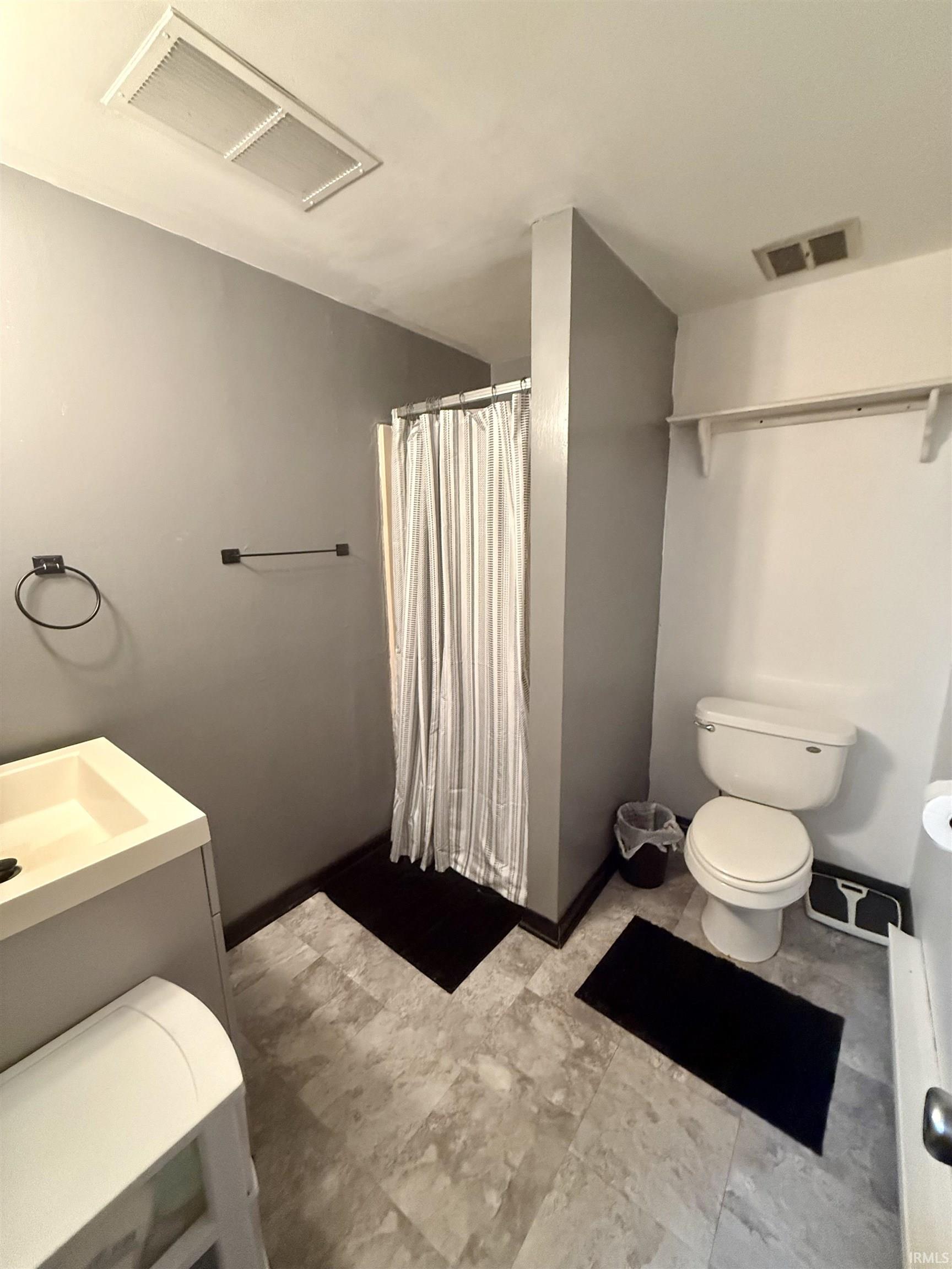 Bathroom featuring a vanity with integrated sink, shower with curtain, toilet, and light-toned tile-pattern flooring